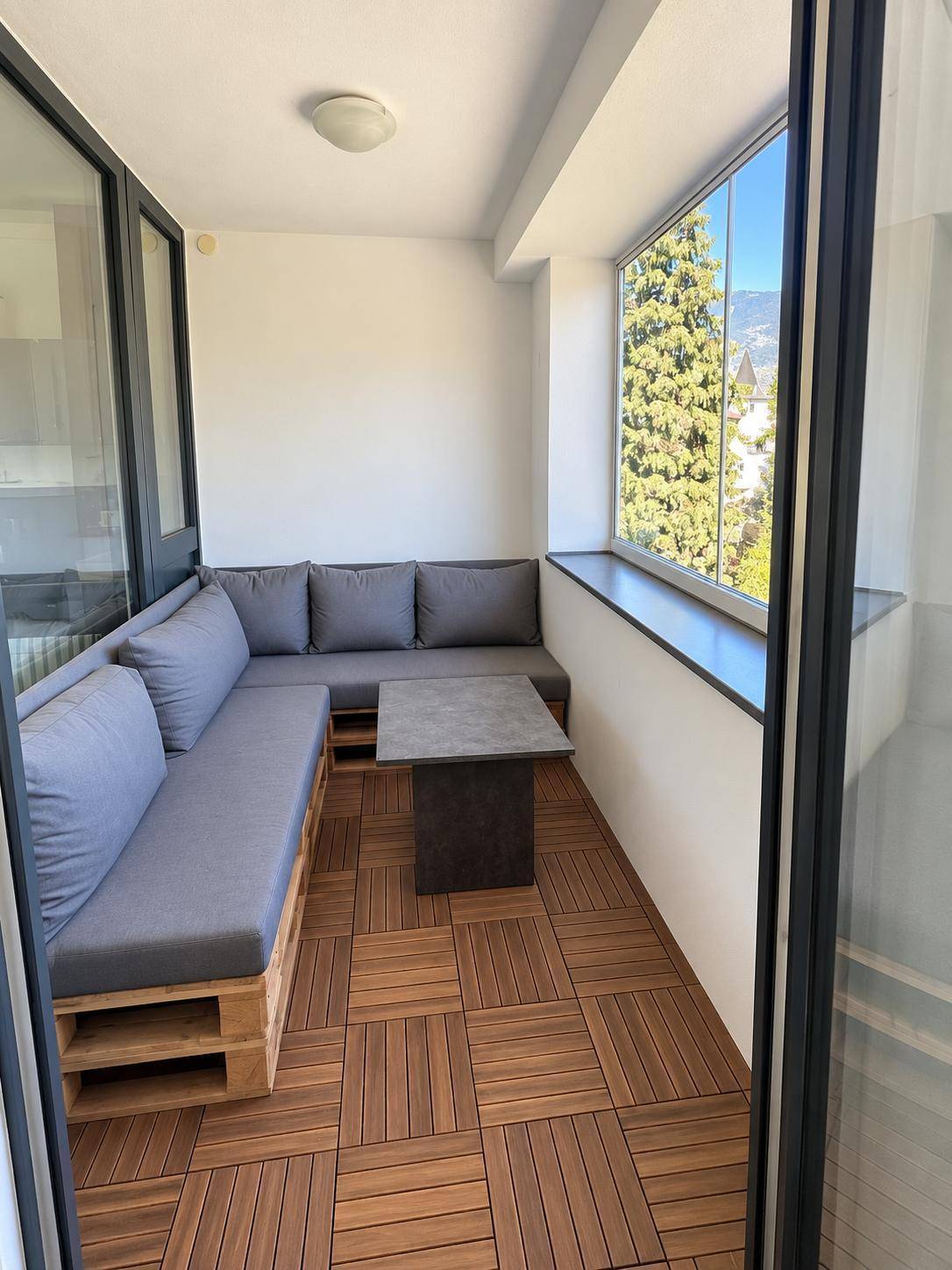 Gemütliche Loggia mit Palettenmöbeln, Holzbodenfliesen und weitem Blick ins Grüne.