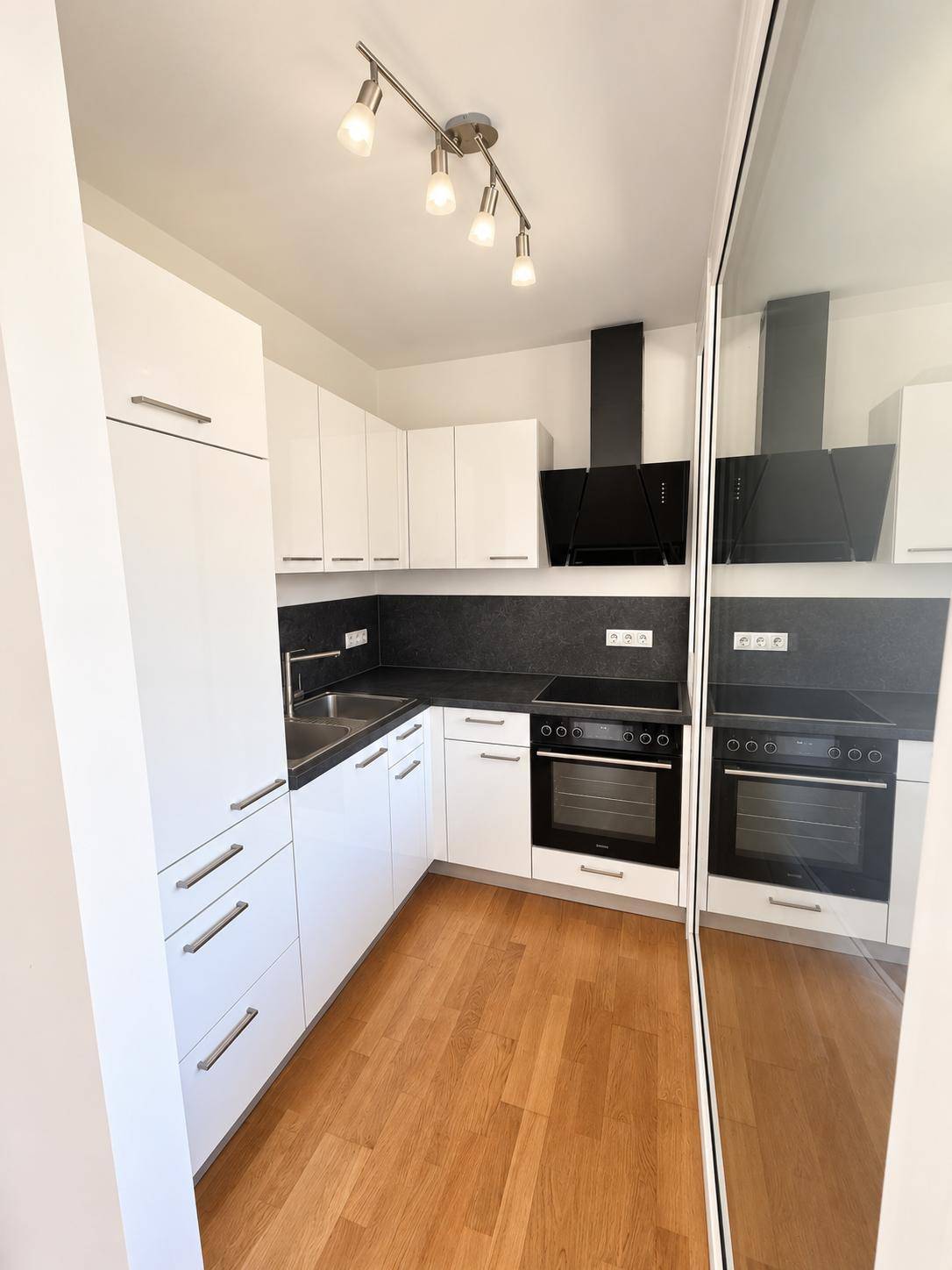 Moderne Einbauküche mit weißen Schränken, dunkler Arbeitsplatte und integrierten Geräten.