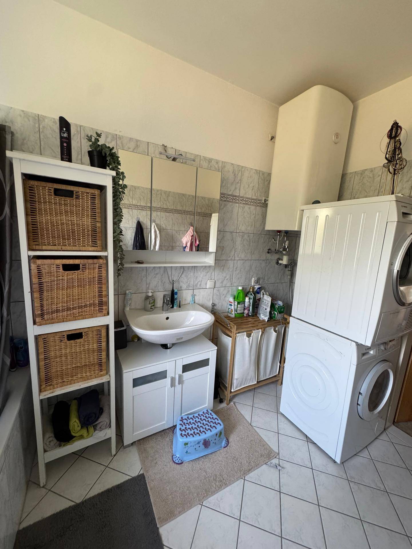 Badezimmer mit Waschbecken, Waschmaschine und Trockner, gefliest und praktisch eingerichtet.