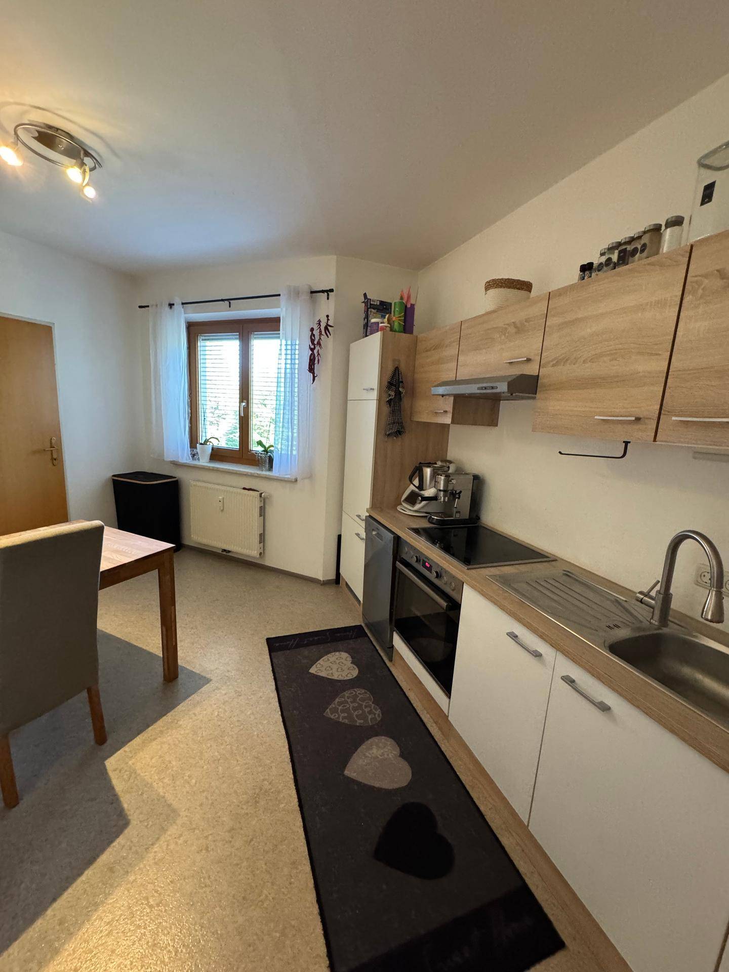 Funktionale Küche mit hellen Holzfronten, Essbereich und Fenster für natürliches Licht.