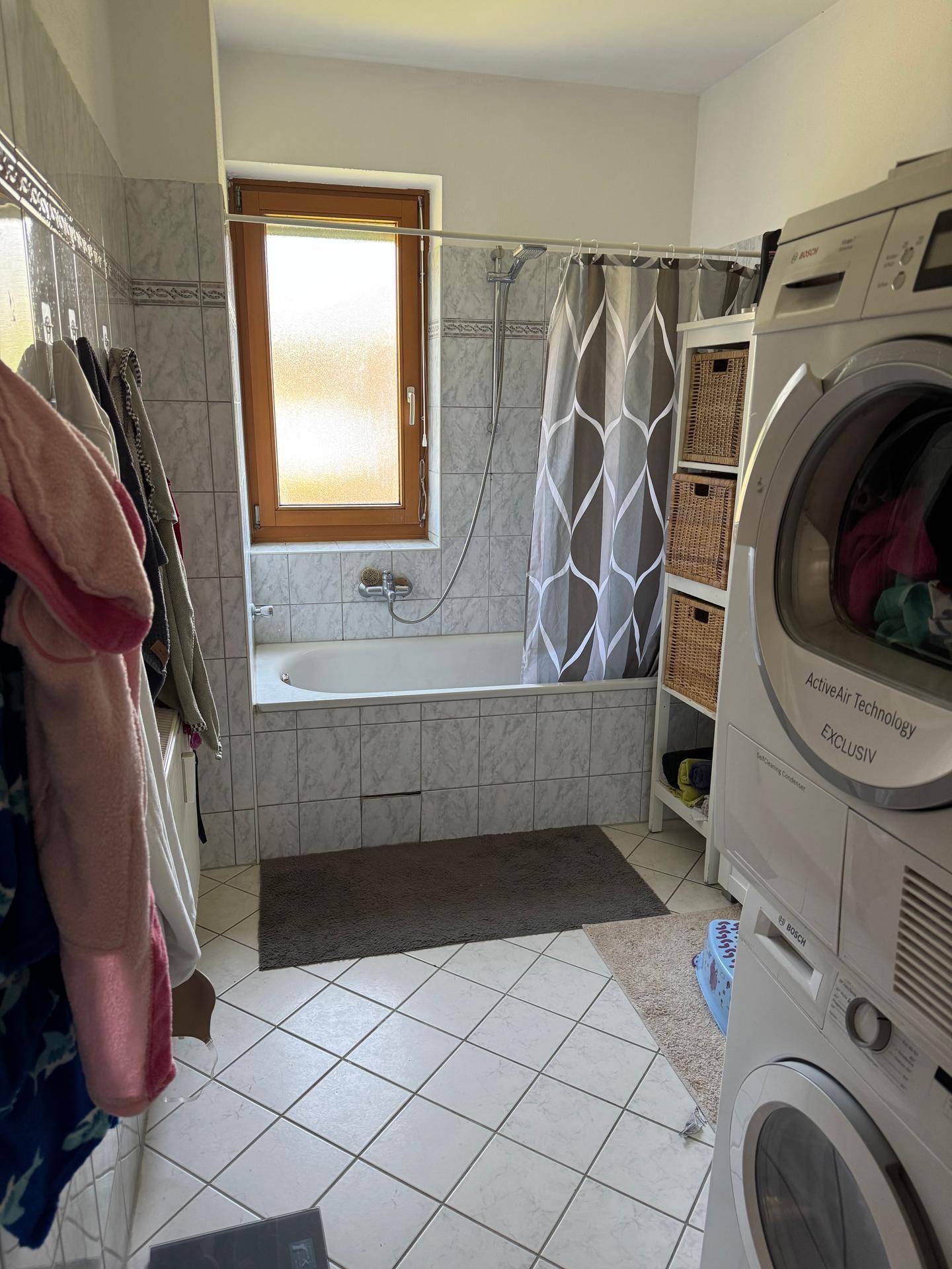 Badezimmer mit Badewanne, Duschvorhang und Fenster, hell gefliest und funktional.