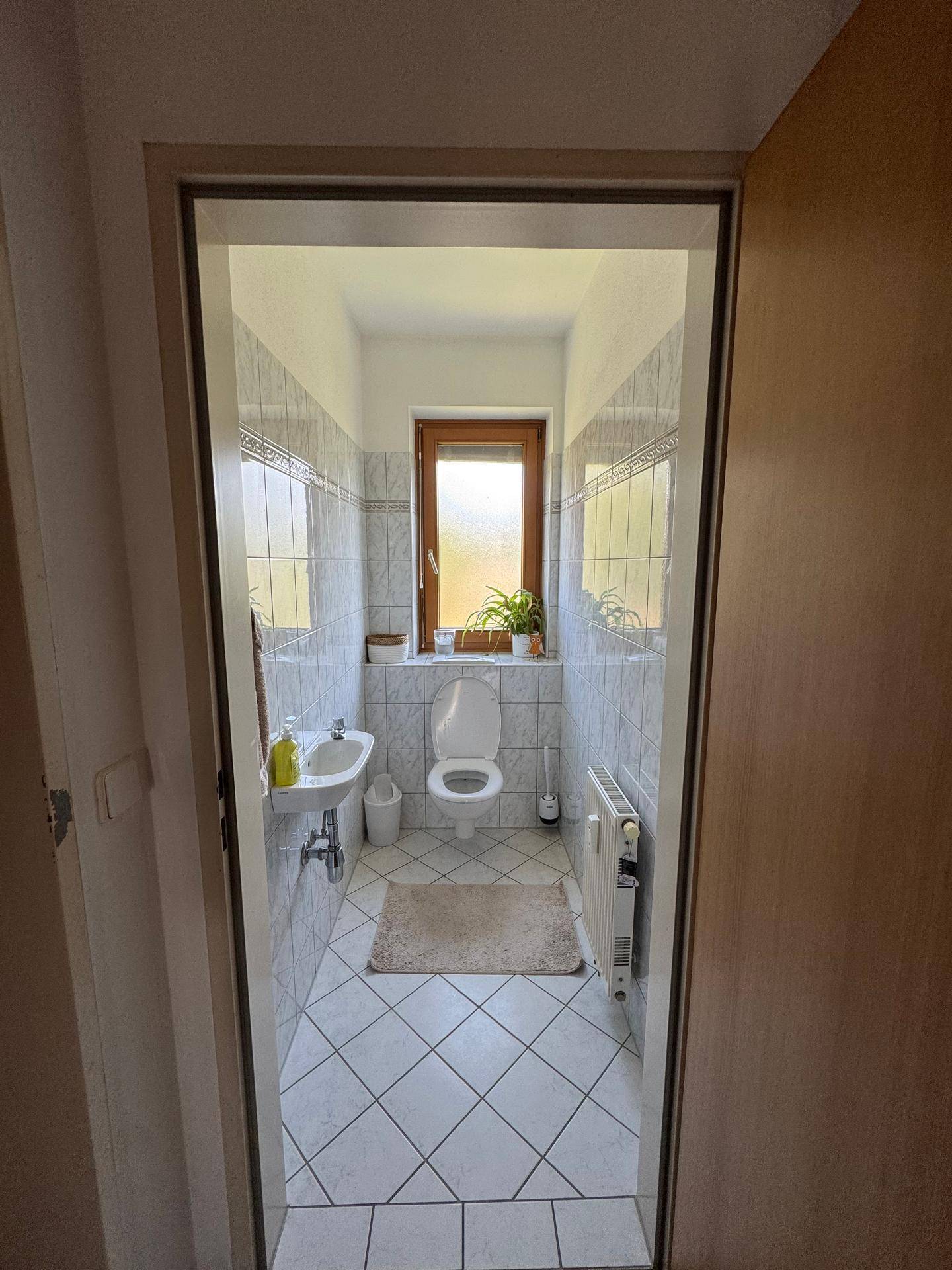 Separates WC mit Fenster, Waschbecken und Wandfliesen, hell und sauber.