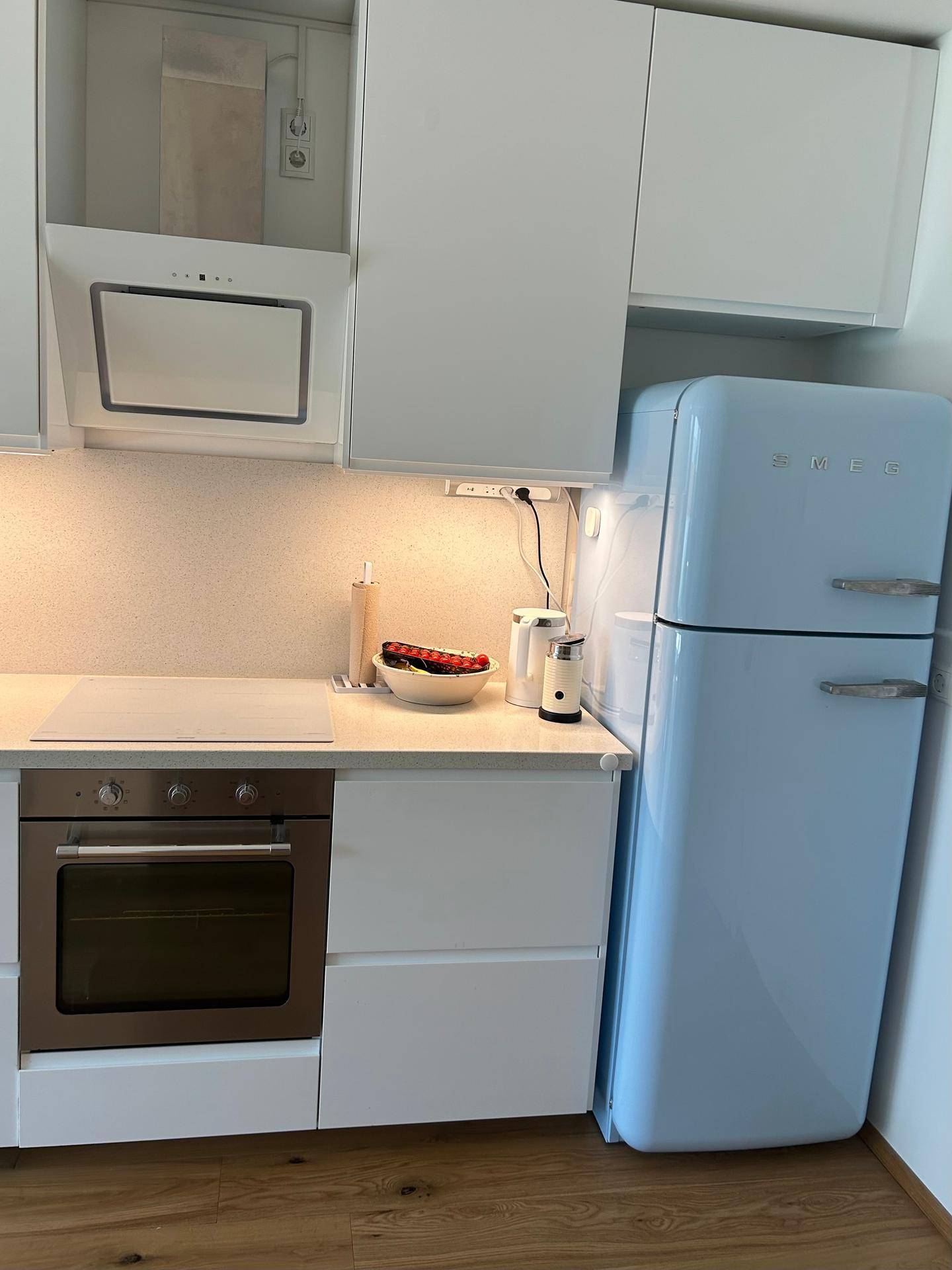Detailansicht der modernen Küche mit Induktionskochfeld, Backofen und einem stilvollen blauen Kühlschrank.