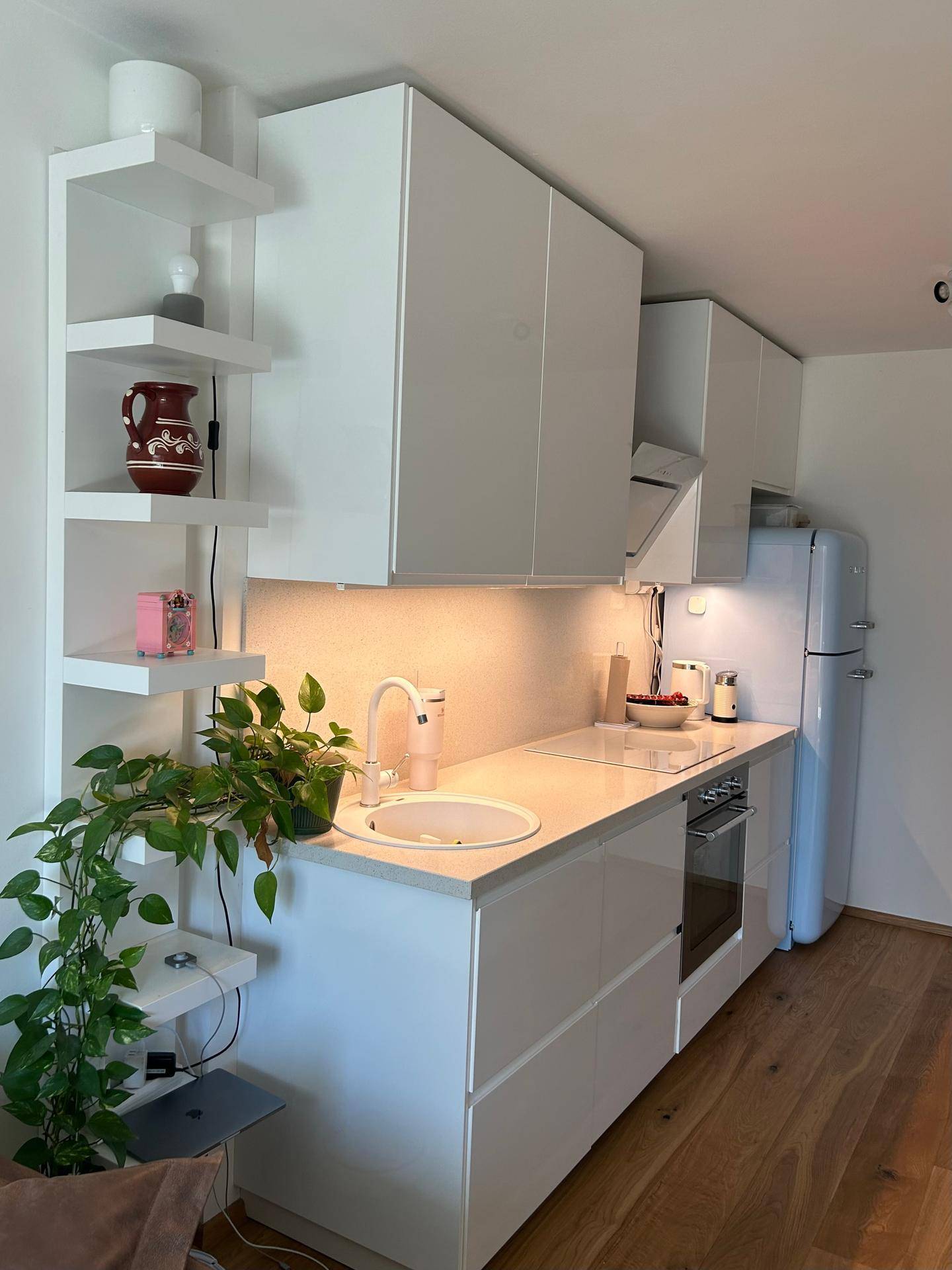 Moderne Küchenzeile mit weißen Hochglanzschränken, Holzboden und einem auffälligen blauen Kühlschrank.