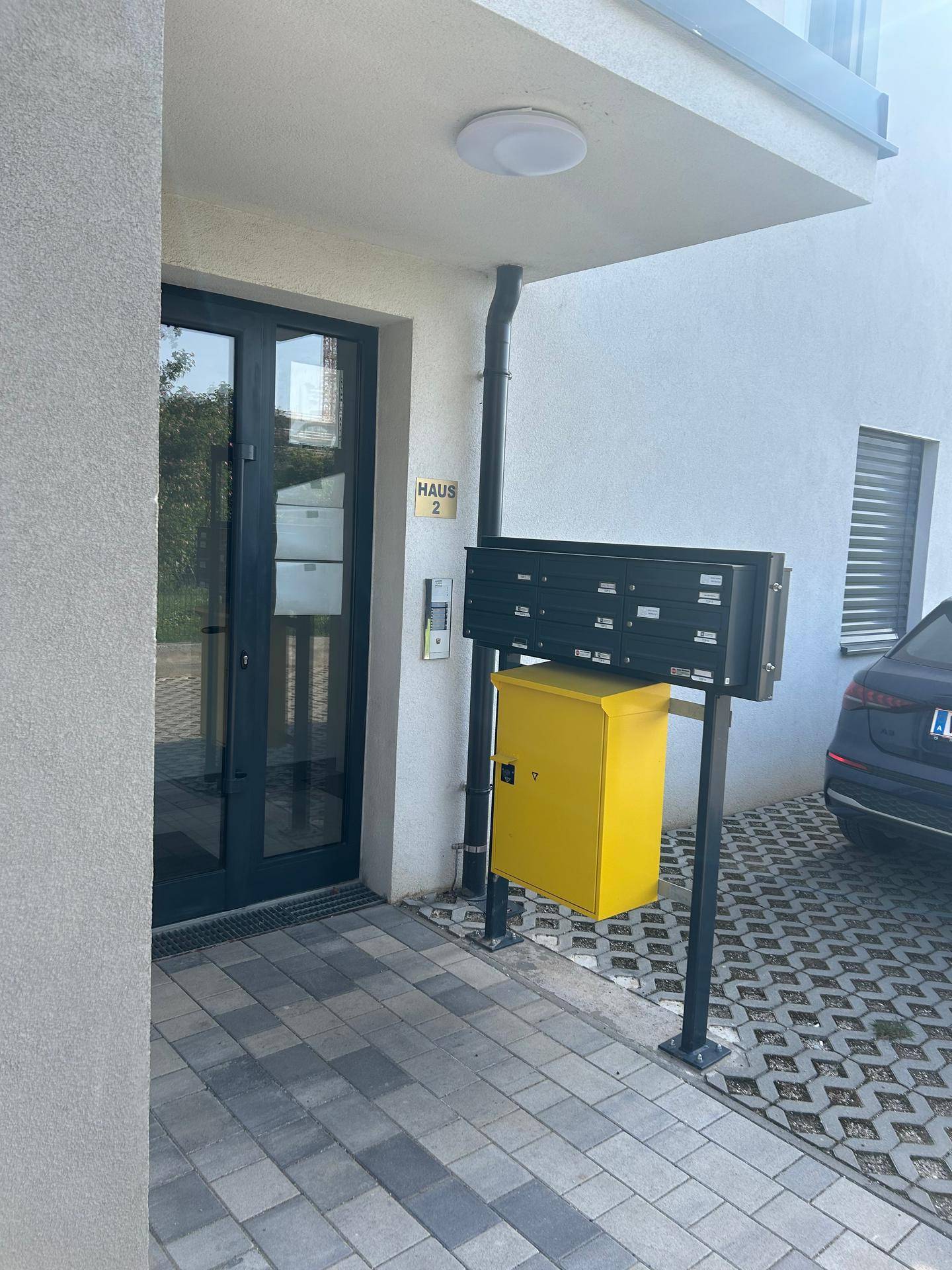 Eingangsbereich eines modernen Gebäudes mit Briefkästen und einer gelben Paketbox.