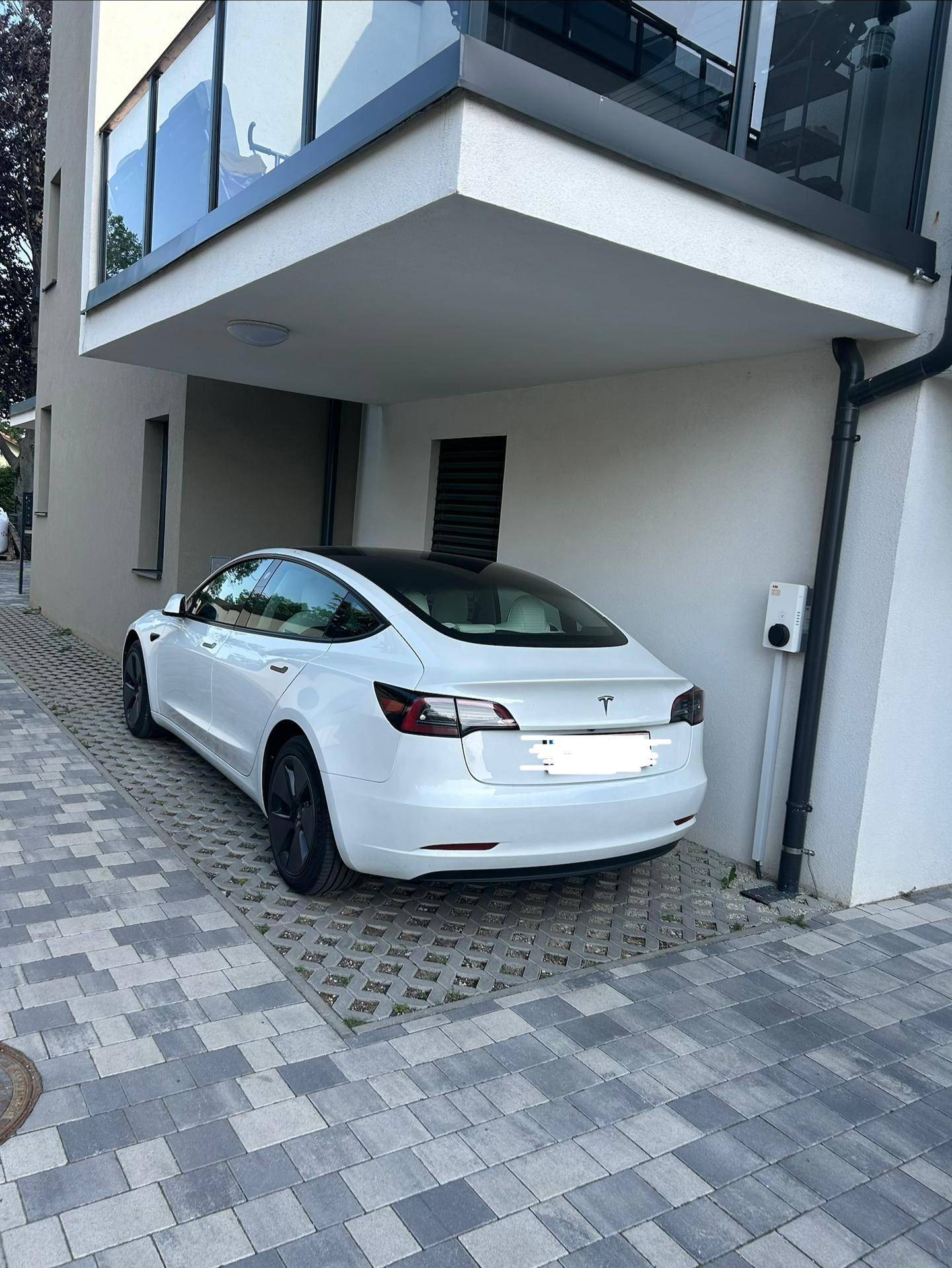 Weißes Tesla-Fahrzeug parkt unter einem Gebäudeüberhang mit einer Ladestation für Elektroautos.