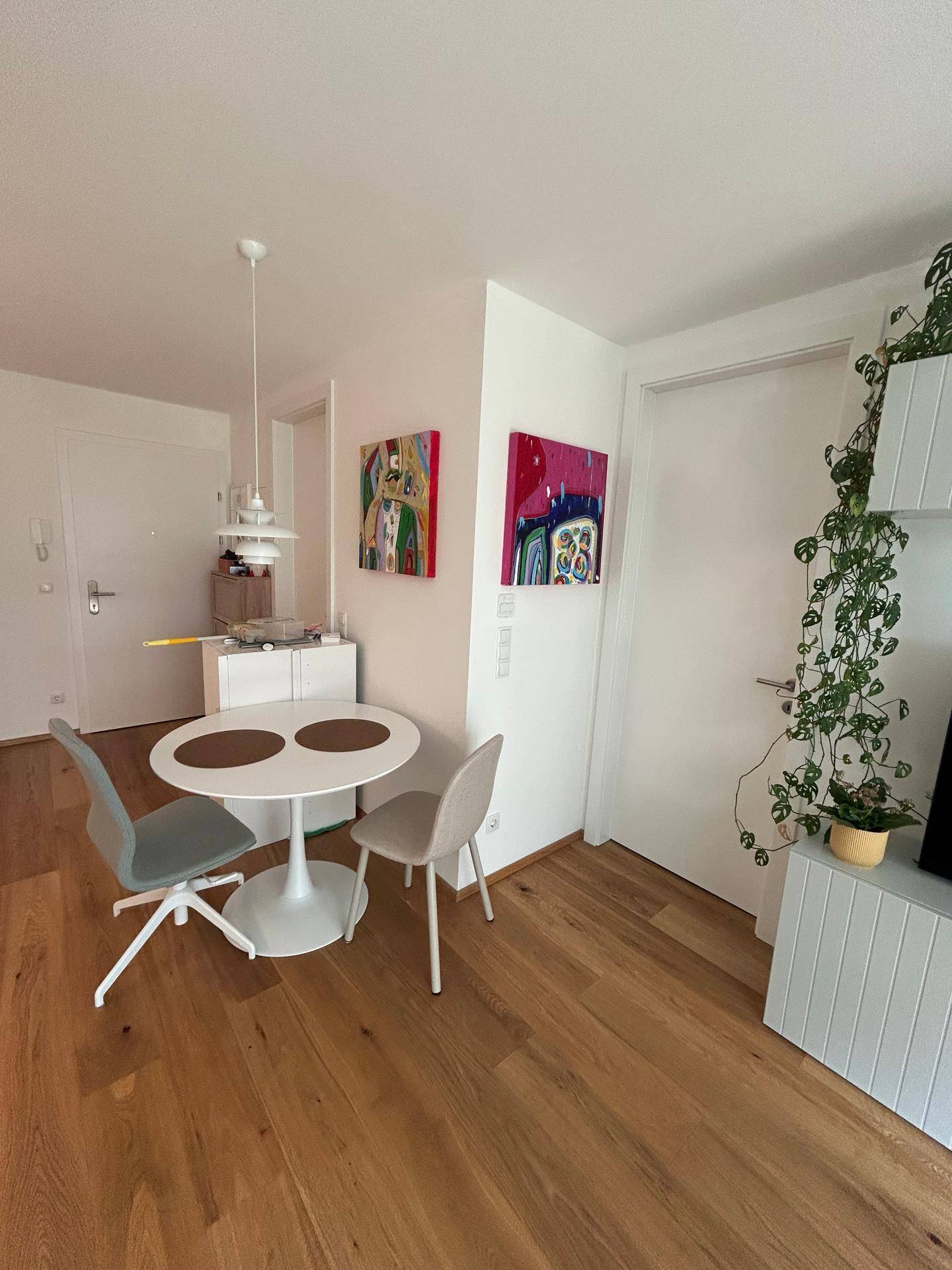 Gemütlicher Essbereich mit rundem Tisch, zwei Stühlen und farbenfrohen Kunstwerken an der Wand.