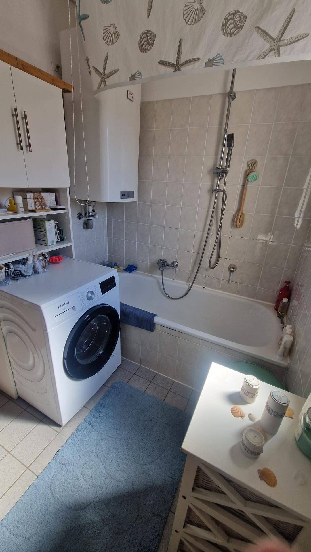 Badezimmer mit Badewanne, Duschfunktion und Waschmaschine, hell gefliest.