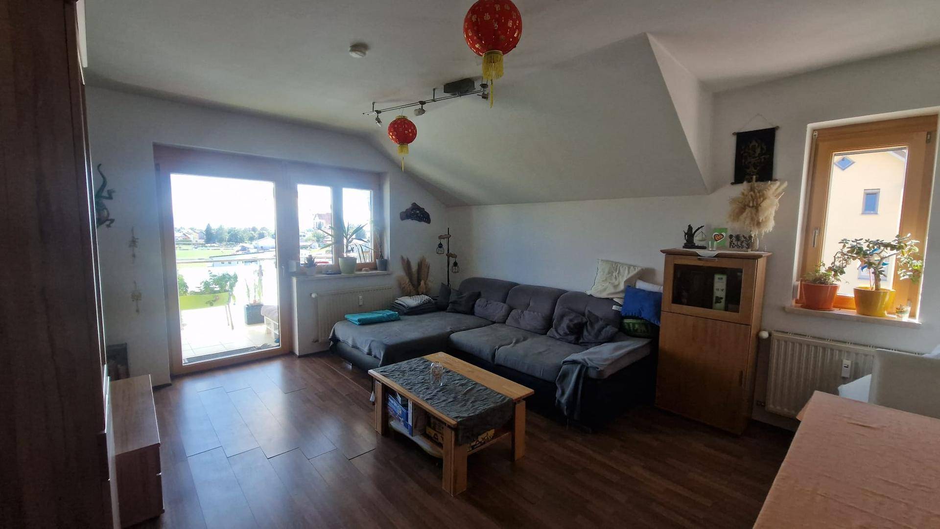 Helles Wohnzimmer mit Holzboden, gemütlichem Sofa und Zugang zu einem Balkon.