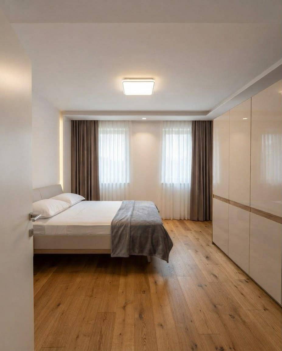 Helles Schlafzimmer mit Holzboden, großem Bett und glänzenden Einbauschränken.