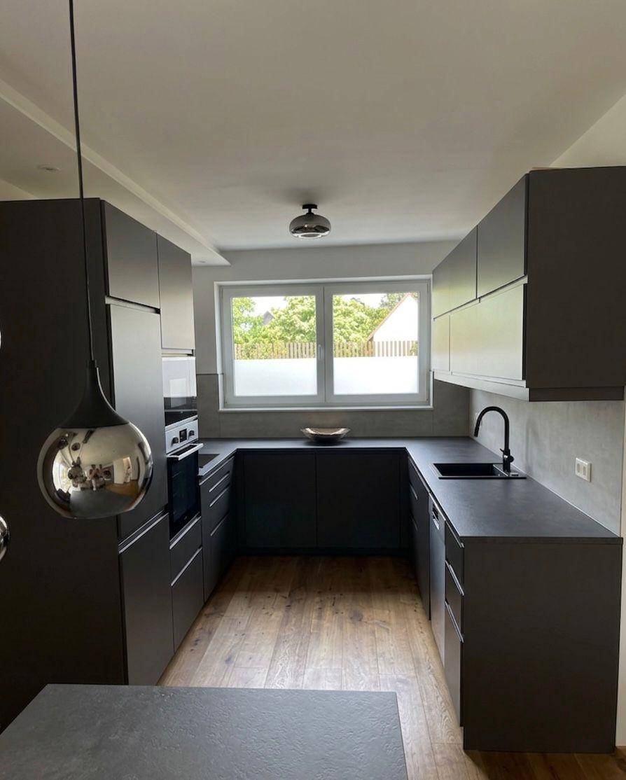 Moderne U-förmige Küche mit dunklen Schränken, integrierten Geräten und Fensterblick.