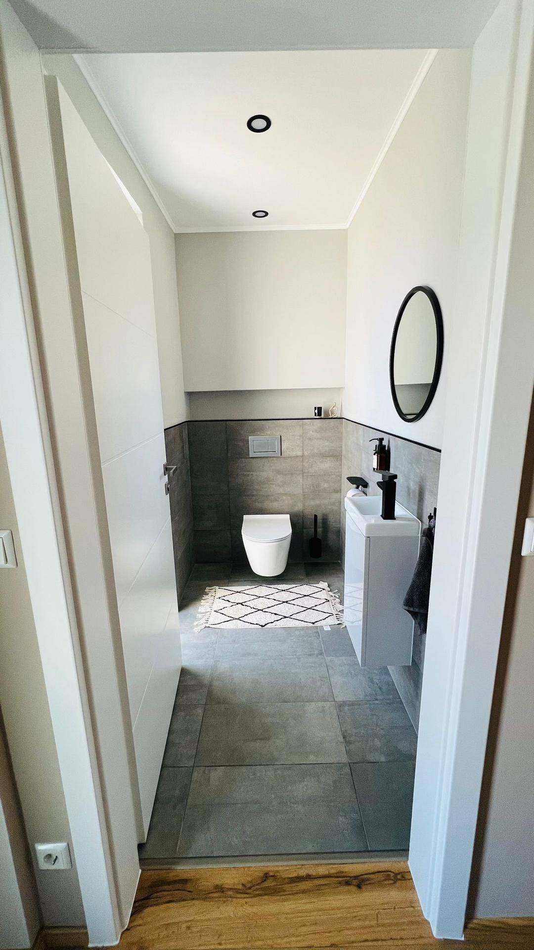 Modernes Gäste-WC mit Wand-WC, kleinem Waschbecken und grauen Fliesen.