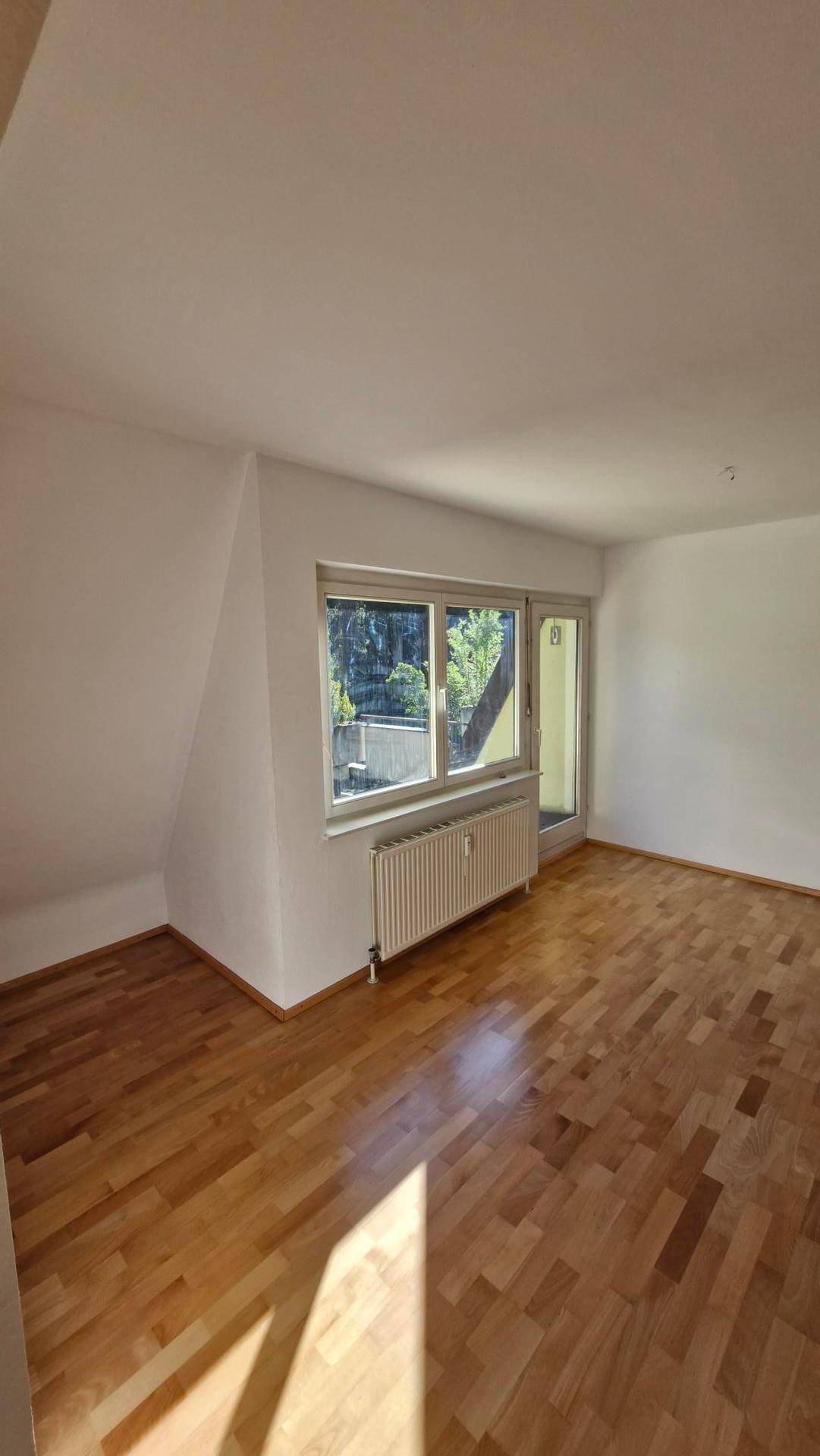 Geräumiges Zimmer mit Parkettboden, Heizkörper und Zugang zu einem Außenbereich.