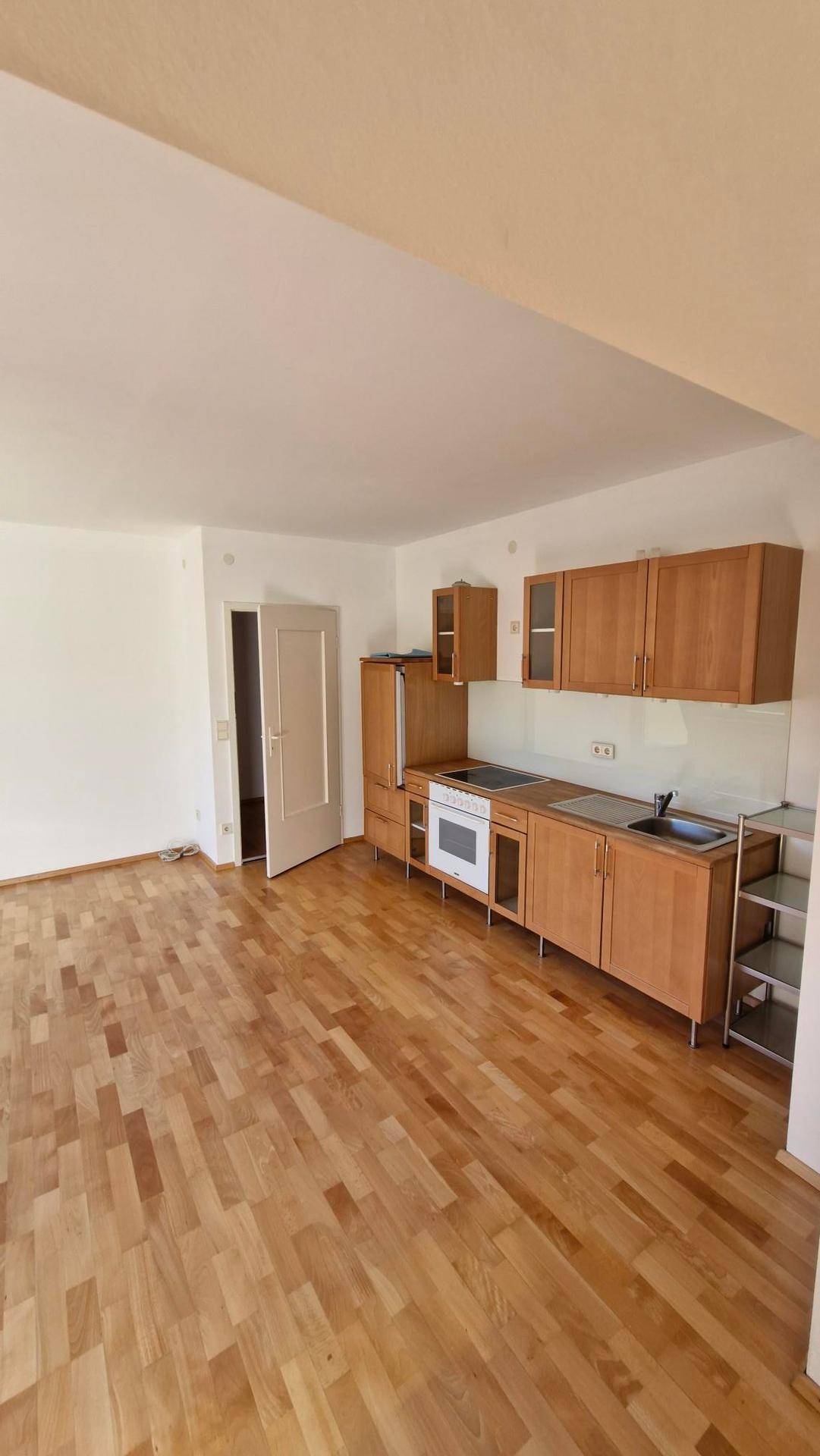 Offener Raum mit Parkettboden und einer einfachen Einbauküche entlang der Wand.