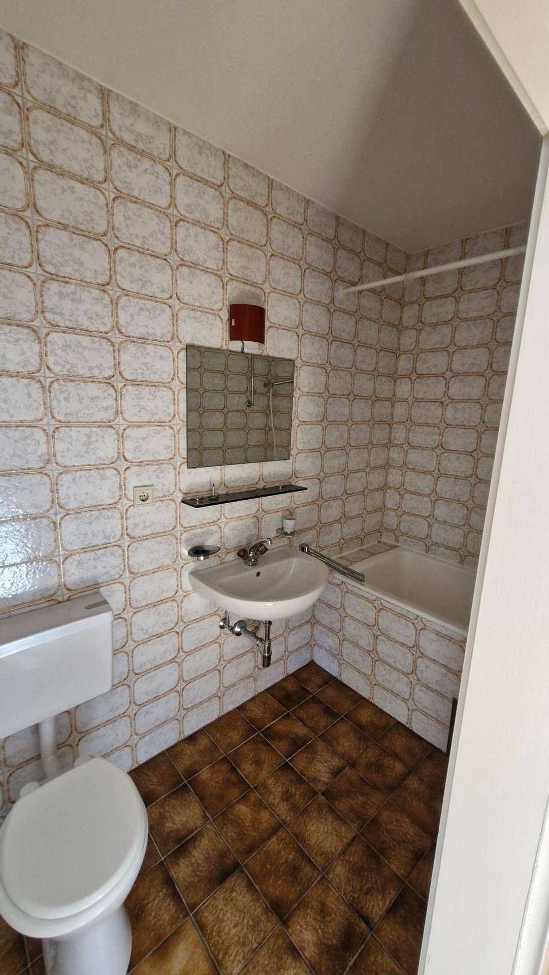 Kleines Badezimmer mit gemusterten Fliesen, Toilette, Waschbecken und Badewanne.
