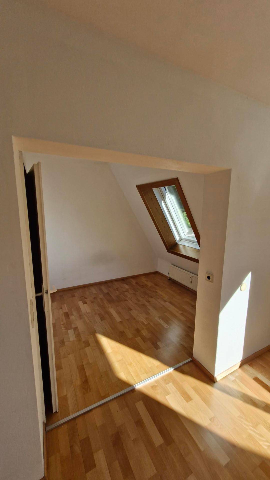 Heller Raum mit Parkettboden und Dachfenster, der viel Tageslicht hereinlässt.