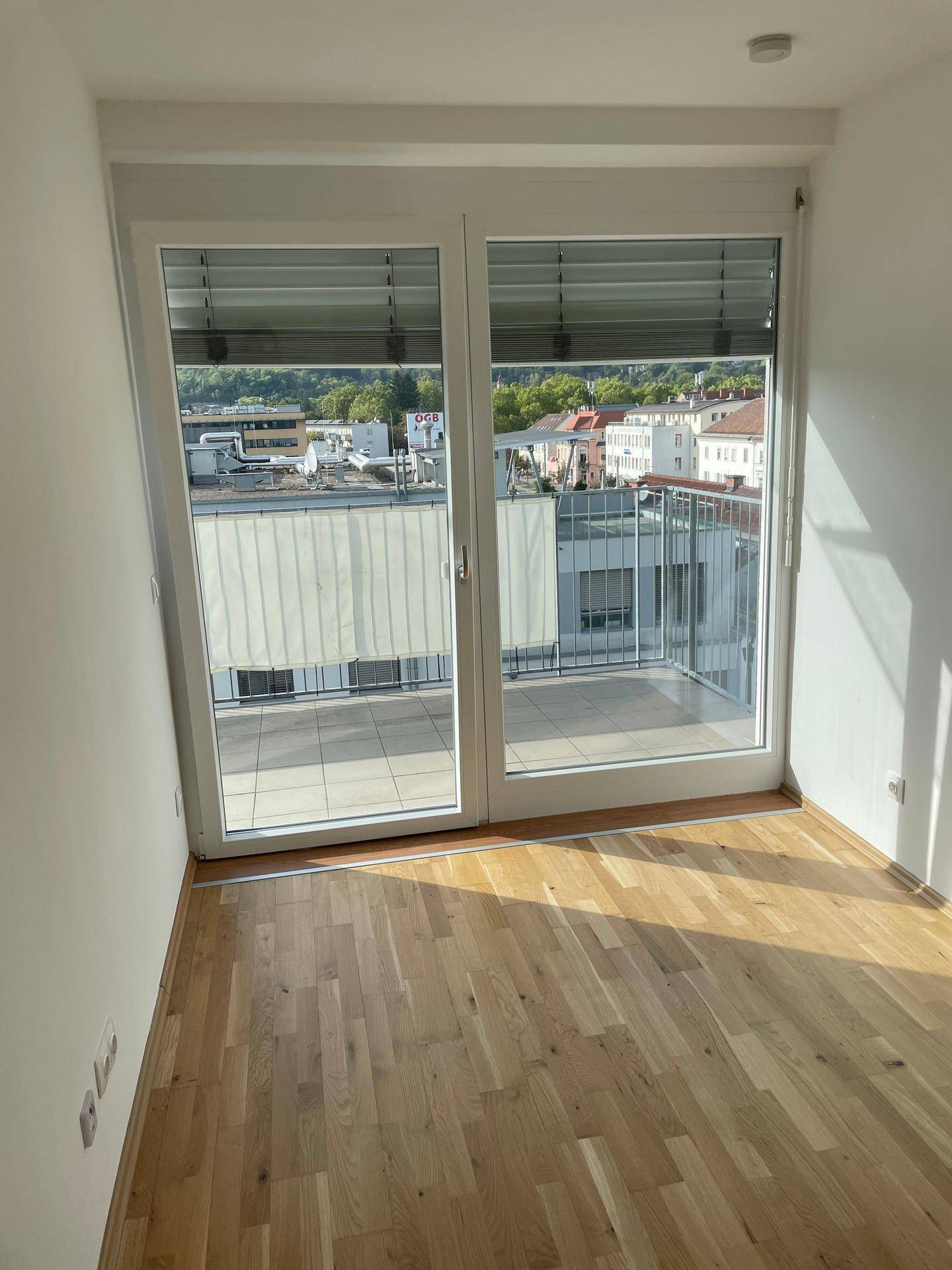 Lichtdurchflutetes Schlafzimmer mit Parkettboden und großen Fenstern, die auf einen Balkon führen.
