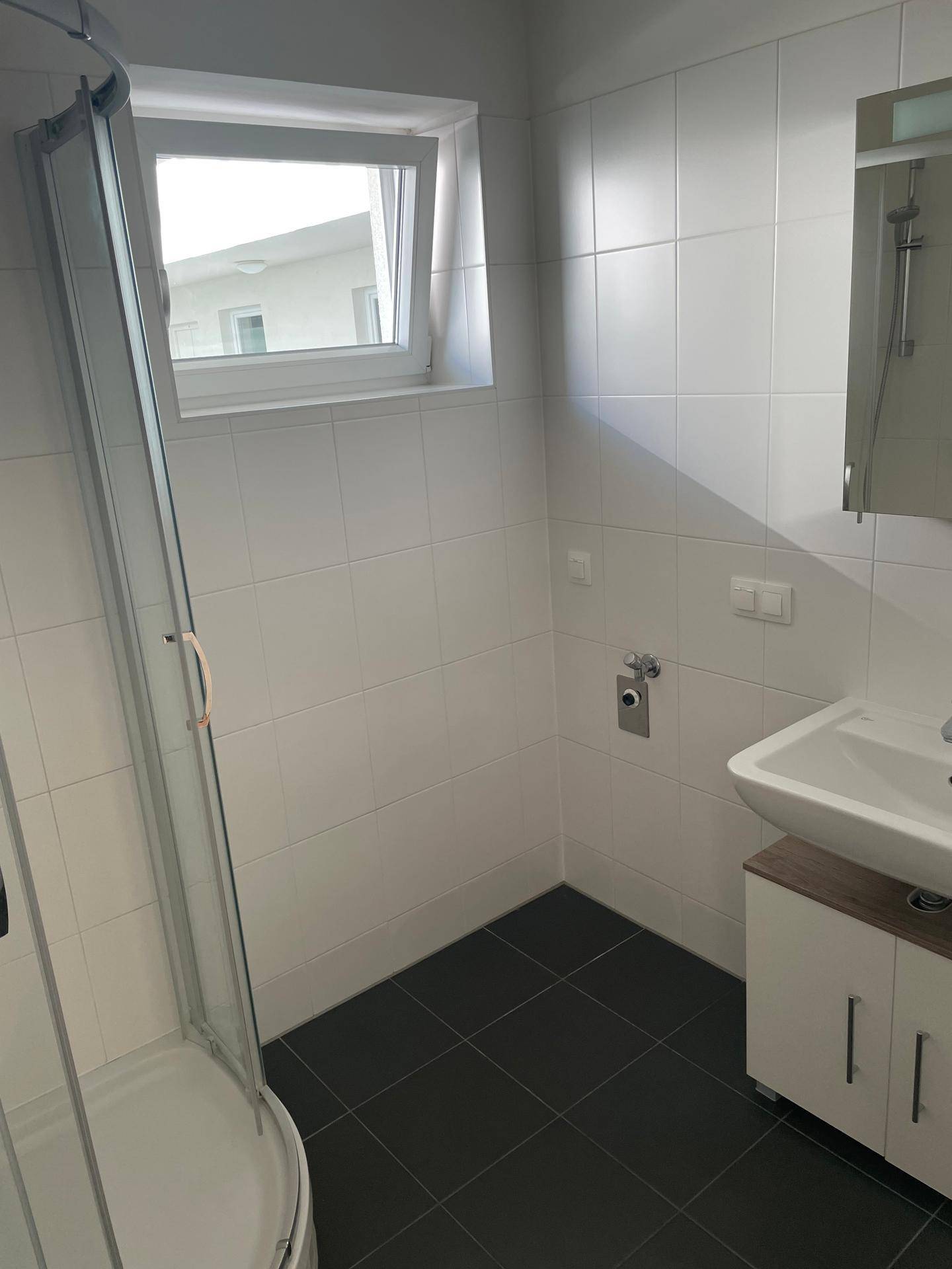 Modernes Badezimmer mit Dusche, Waschbeckenunterschrank und Fenster für natürliches Tageslicht.