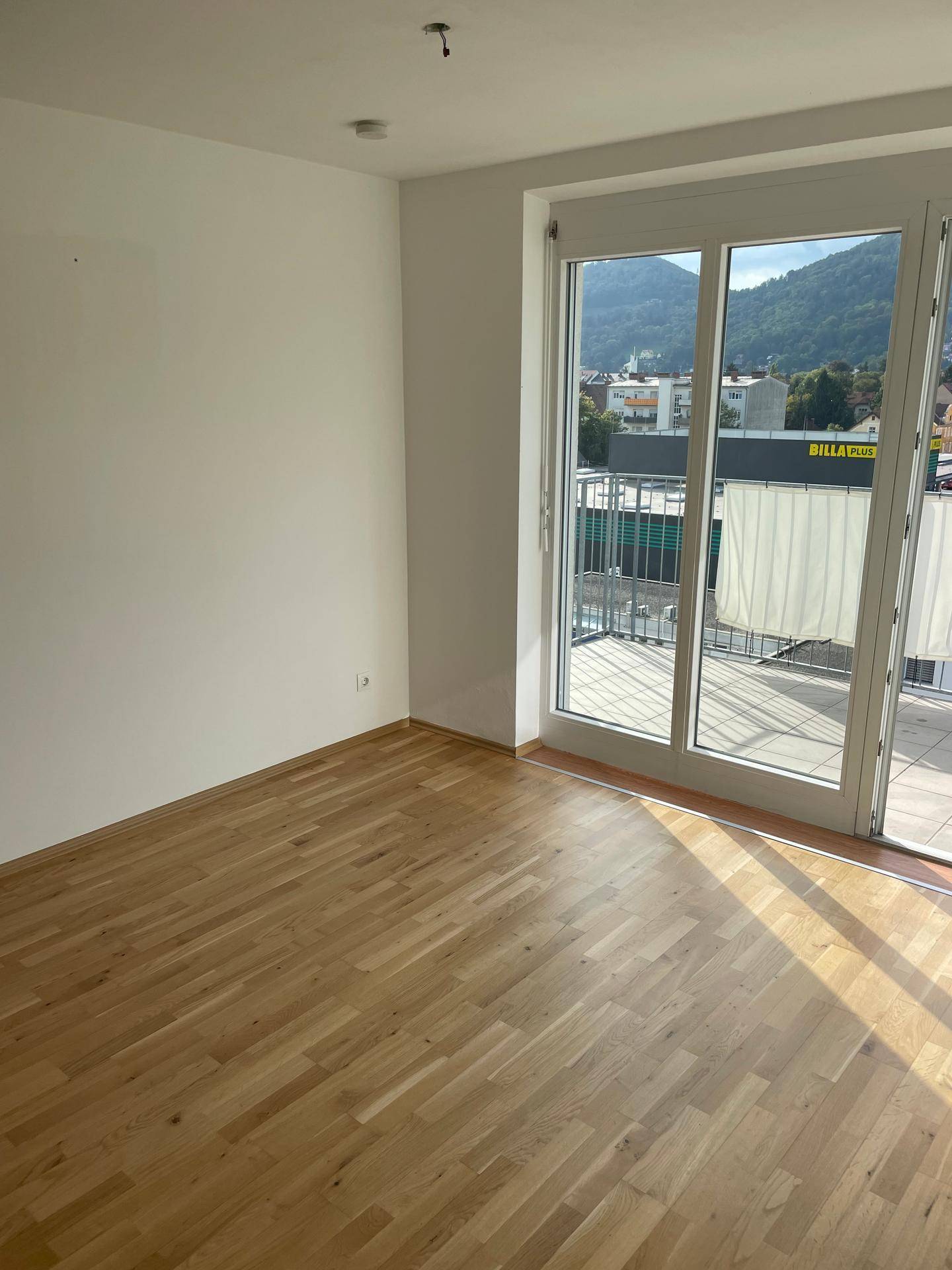 Geräumiges, helles Schlafzimmer mit Holzboden und Blick auf die Stadt und grüne Hügel.