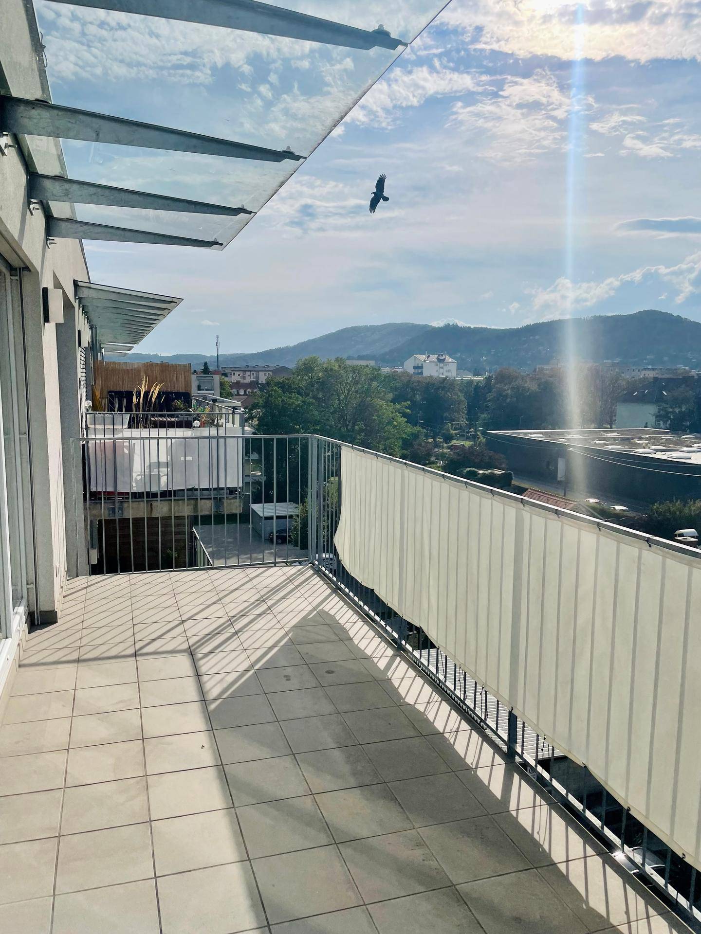 Geräumiger Balkon mit Fliesenboden und Glasüberdachung, bietet einen weiten Blick ins Grüne.