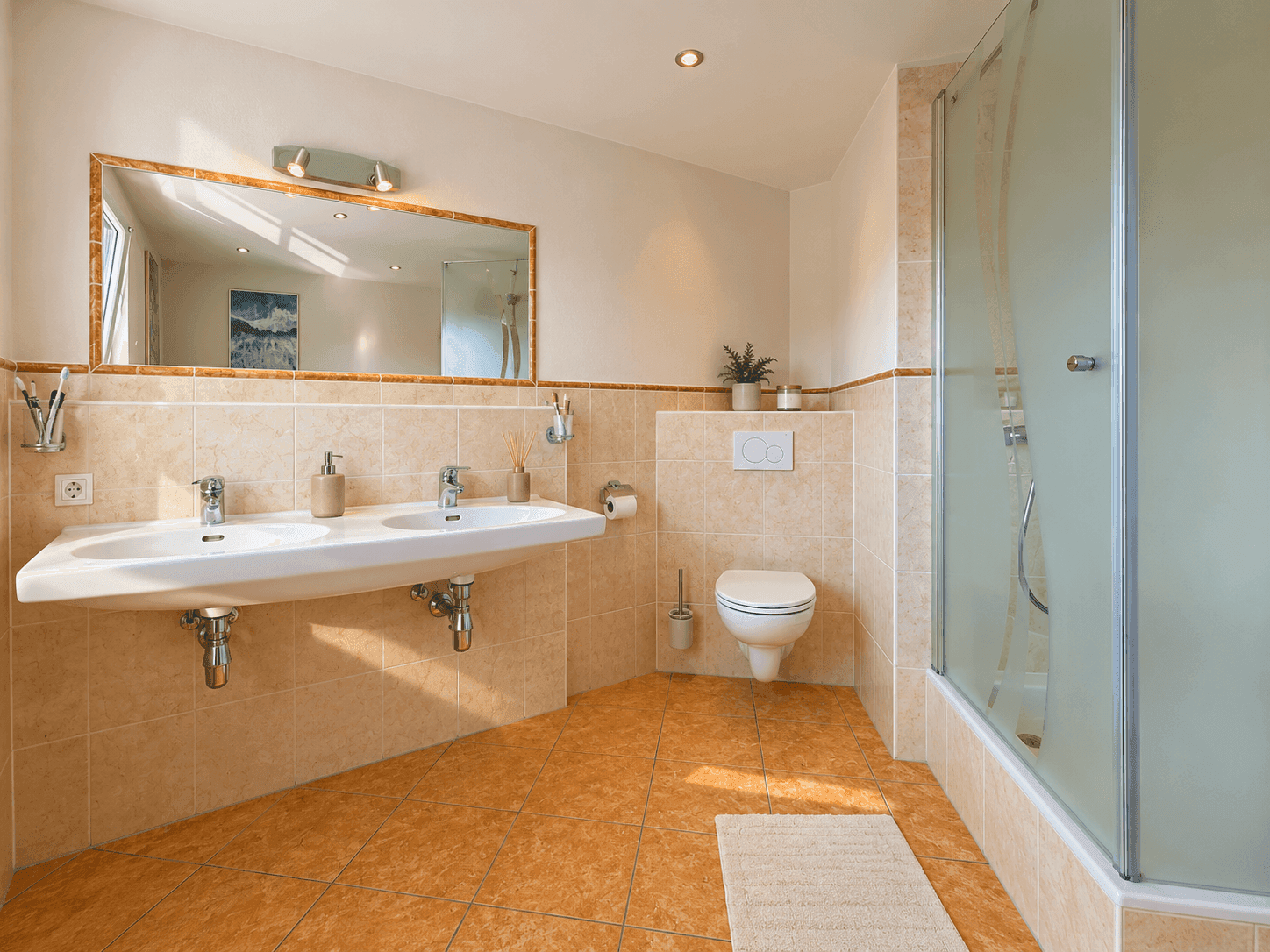 Helles Badezimmer mit Doppelwaschbecken, Toilette und Duschkabine.