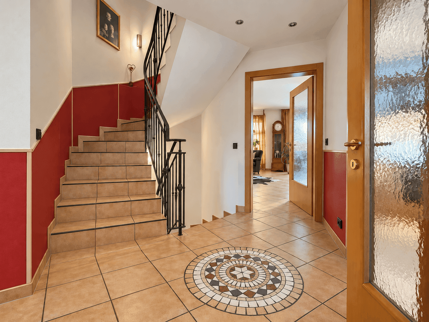 Eingangsbereich mit Treppe, Fliesenboden und dekorativem Mosaik am Boden.