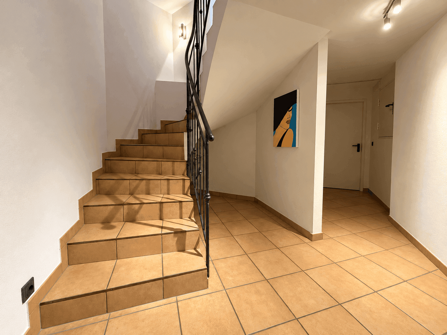 Treppenhaus mit Fliesenstufen und schmiedeeisernem Geländer.