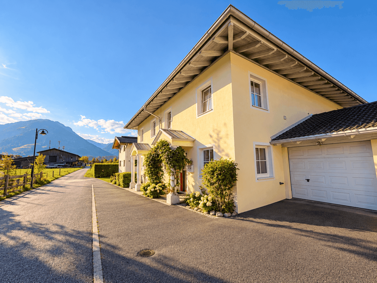 Seitenansicht des Hauses mit Auffahrt, Garage und malerischem Bergblick im Hintergrund.