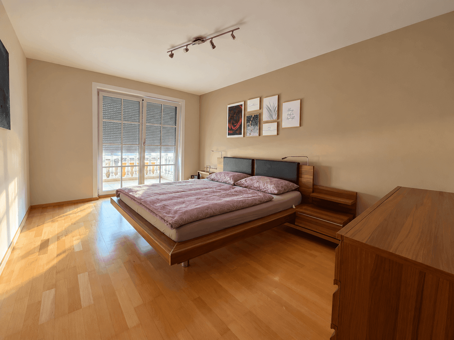 Schlafzimmer mit Holzboden, Doppelbett und Zugang zum Balkon.