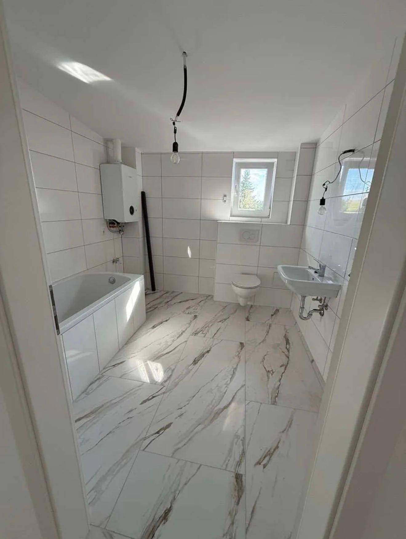 Modernes Badezimmer mit weißen Wandfliesen, Marmoroptik-Bodenfliesen, Badewanne, Toilette und Fenster.