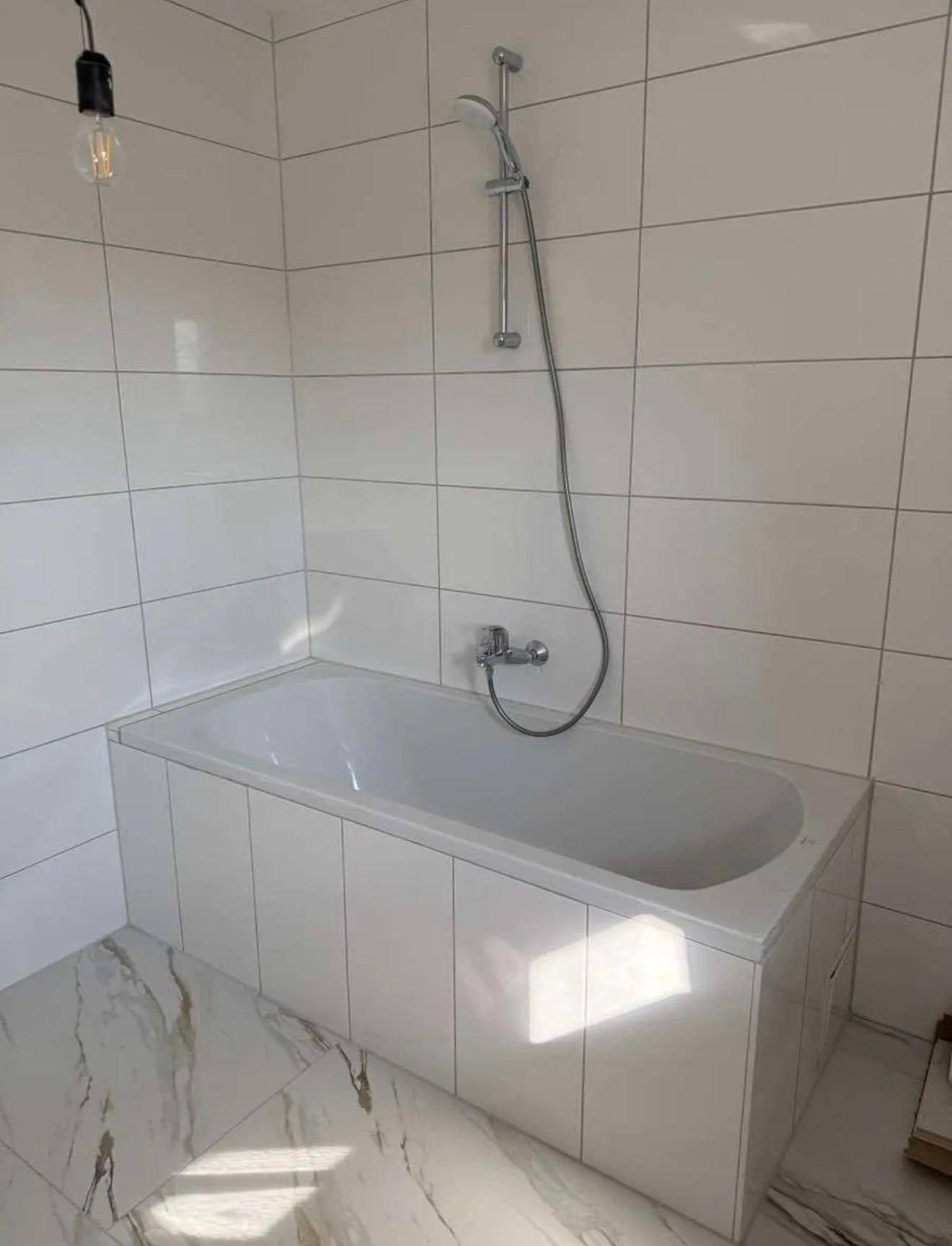 Nahaufnahme einer Badewanne mit Duscharmatur in einem hell gefliesten Badezimmer.