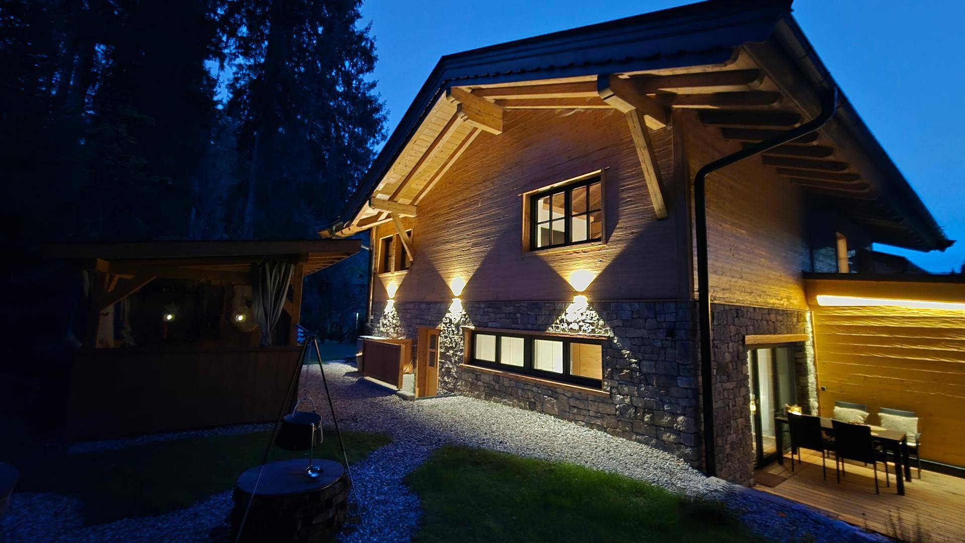 Beleuchtetes Chalet-Haus bei Nacht mit Steinfassade und Holzelementen im Garten.