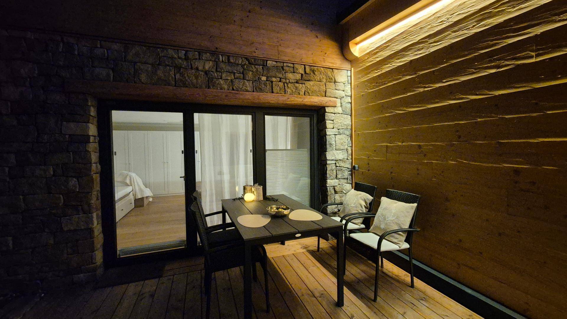 Gemütliche Terrasse am Abend mit Holzboden und Blick in ein Schlafzimmer.
