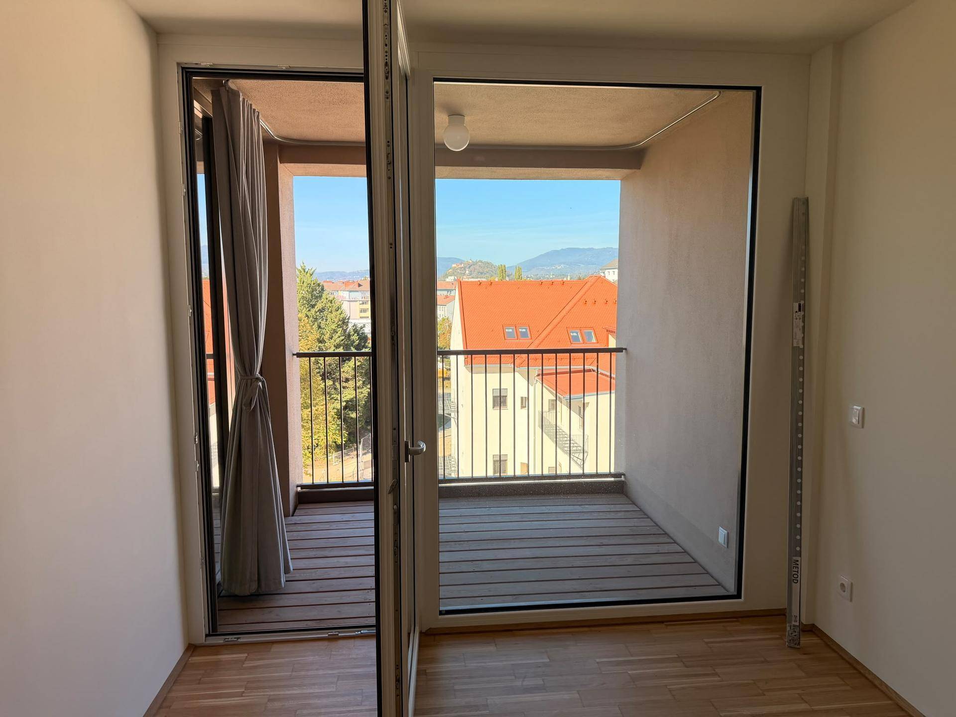 Heller Innenraum mit Zugang zu einem Balkon, der einen Blick auf Dächer und die Umgebung bietet.