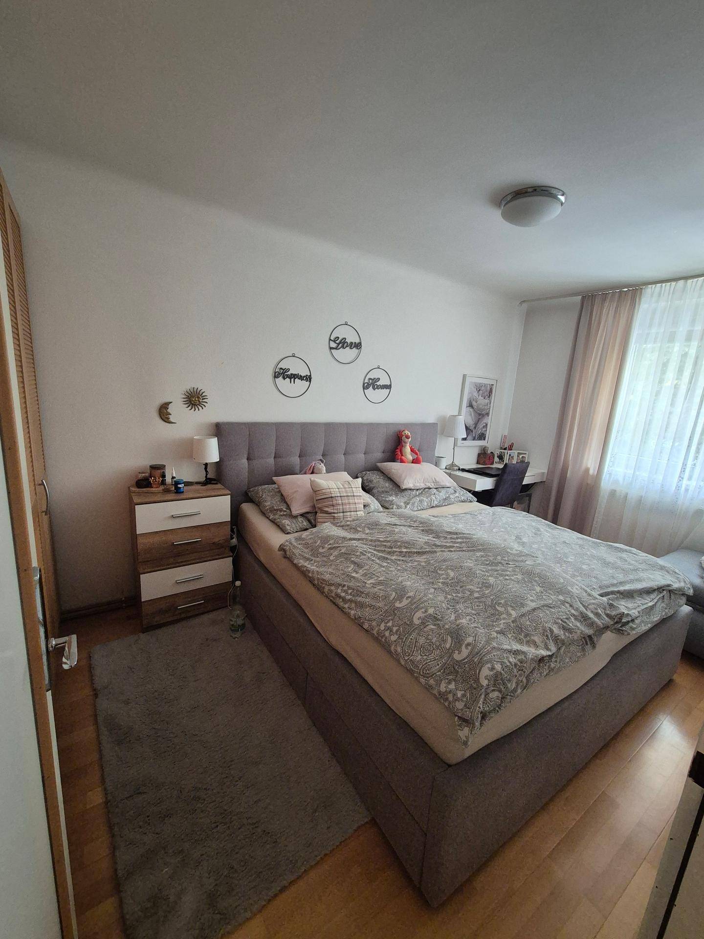 Gemütliches Schlafzimmer mit großem Bett, Holzboden und viel natürlichem Licht durch das Fenster.