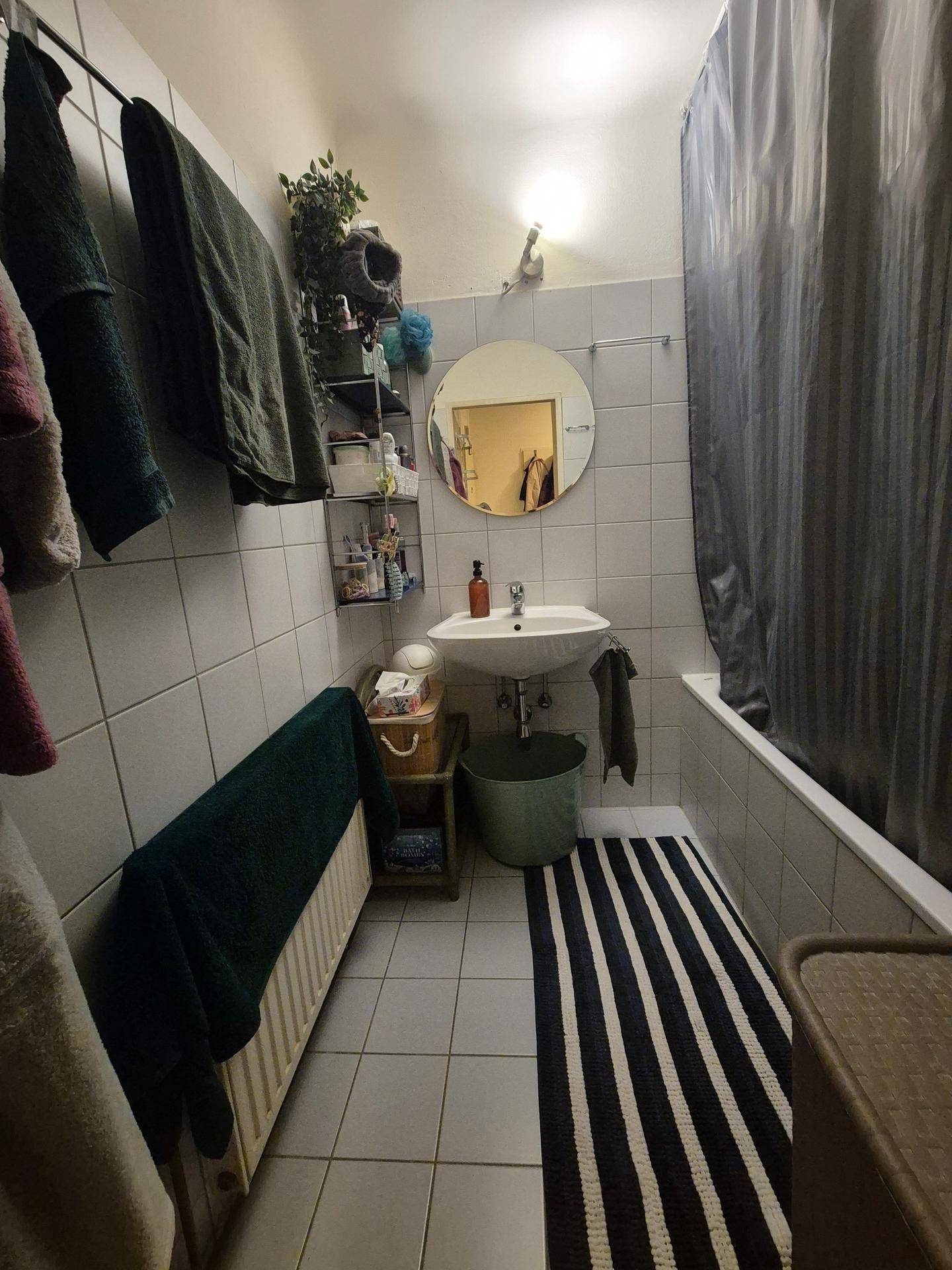 Kleines Badezimmer mit Badewanne, Waschbecken, weißen Fliesen und Handtuchheizkörper.