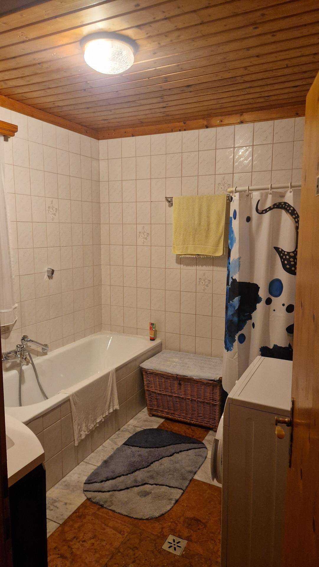 Badezimmer mit Badewanne, Duschvorhang, Waschmaschine und einer Holzdecke.