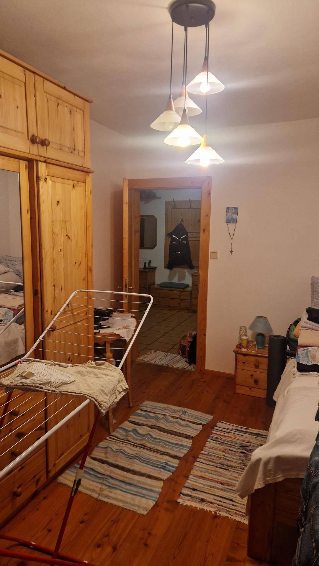 Schlafzimmer mit Holzboden, großem Holzschrank und Blick in einen angrenzenden Raum.