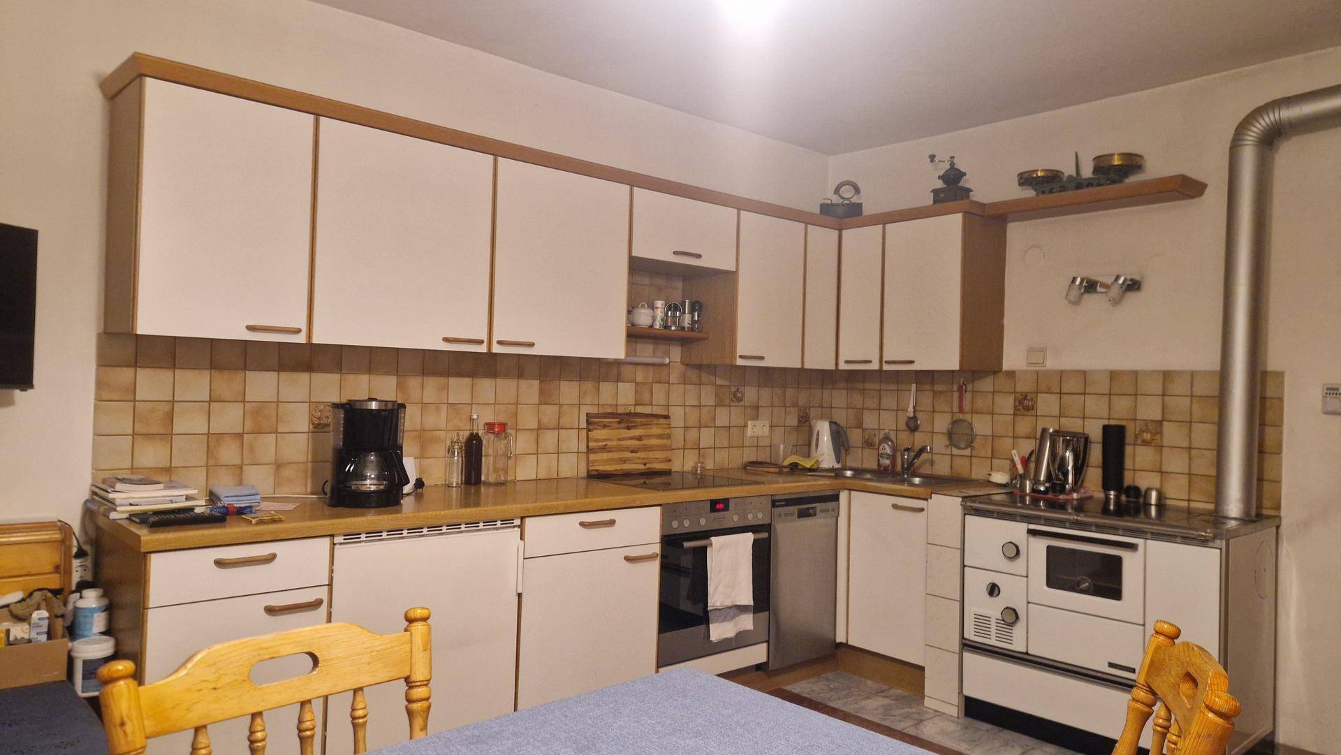 Traditionelle Küche mit weißen Schränken, Fliesenrückwand und einem Holzofen.