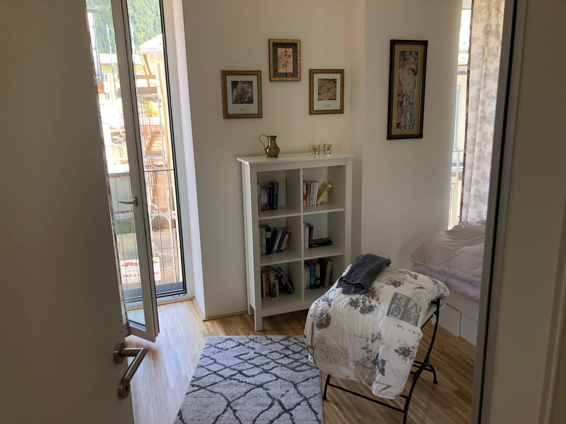 Helles Zimmer mit Bücherregal, Holzboden und Zugang zu einem französischen Balkon.