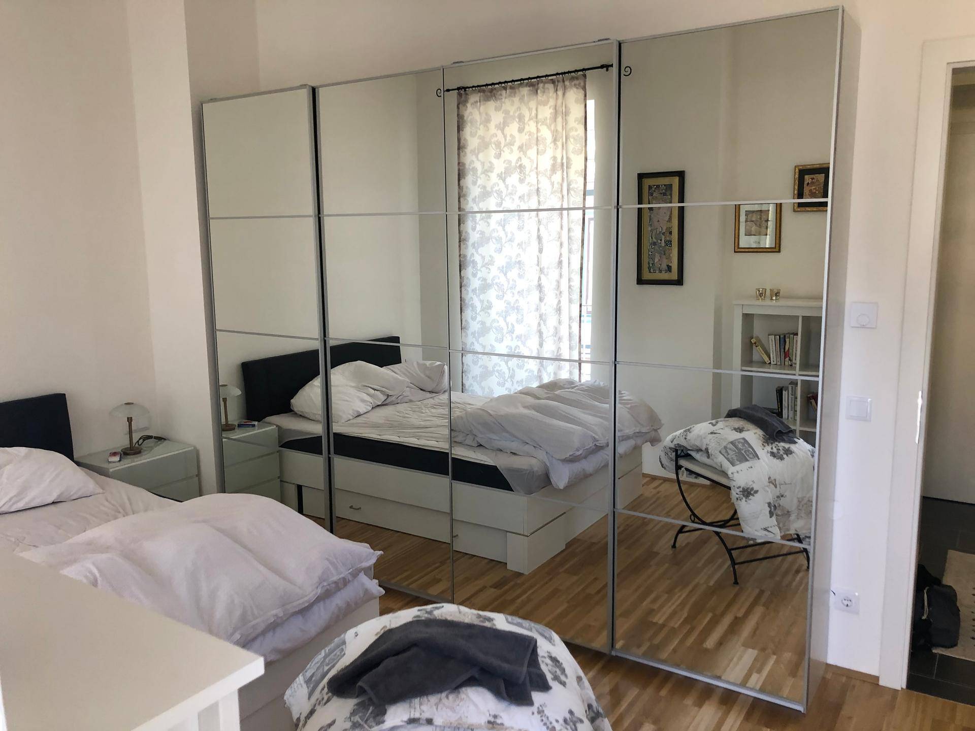 Schlafzimmer mit großem Spiegelschrank, Holzboden und gemütlichem Bett.