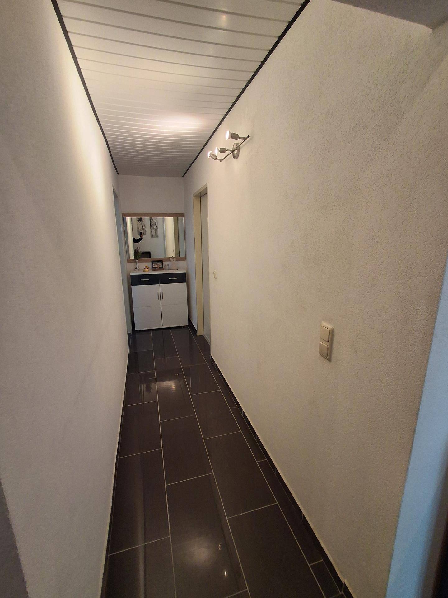 Heller Flur mit dunklem Fliesenboden und einem Spiegel an der Wand.
