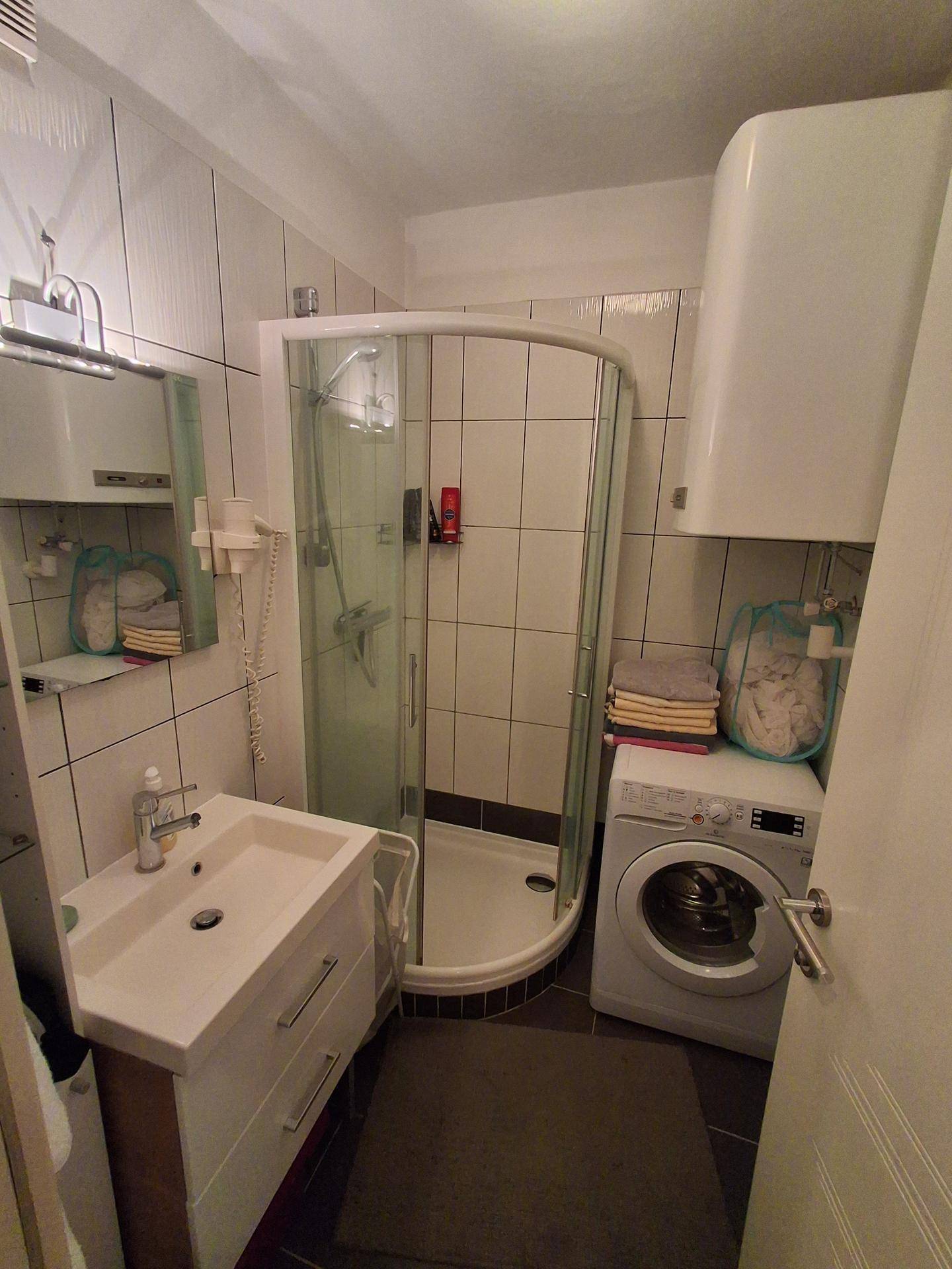 Kleines Badezimmer mit Duschkabine, Waschbecken und integrierter Waschmaschine.
