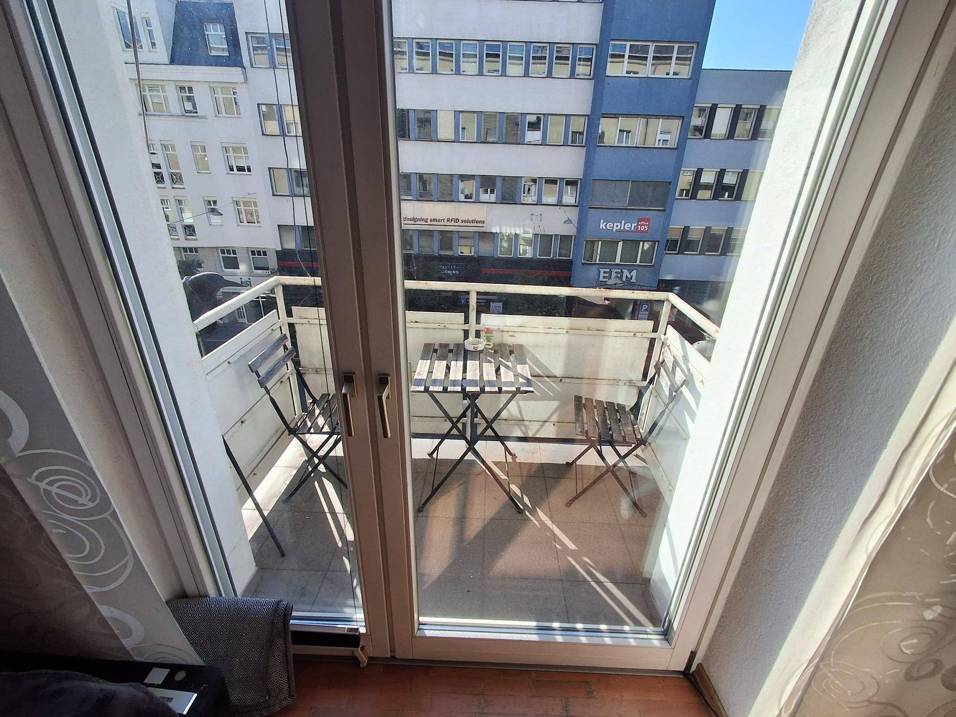 Kleiner Balkon mit Sitzgelegenheiten und Blick auf die umliegenden Gebäude der Stadt.