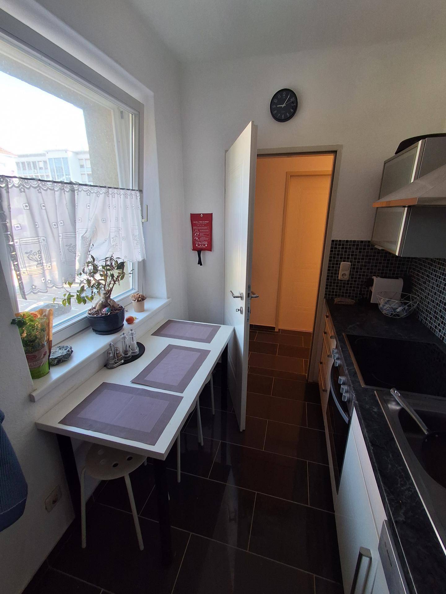 Helle Küche mit Essbereich am Fenster, dunklem Fliesenboden und weißen Schränken.