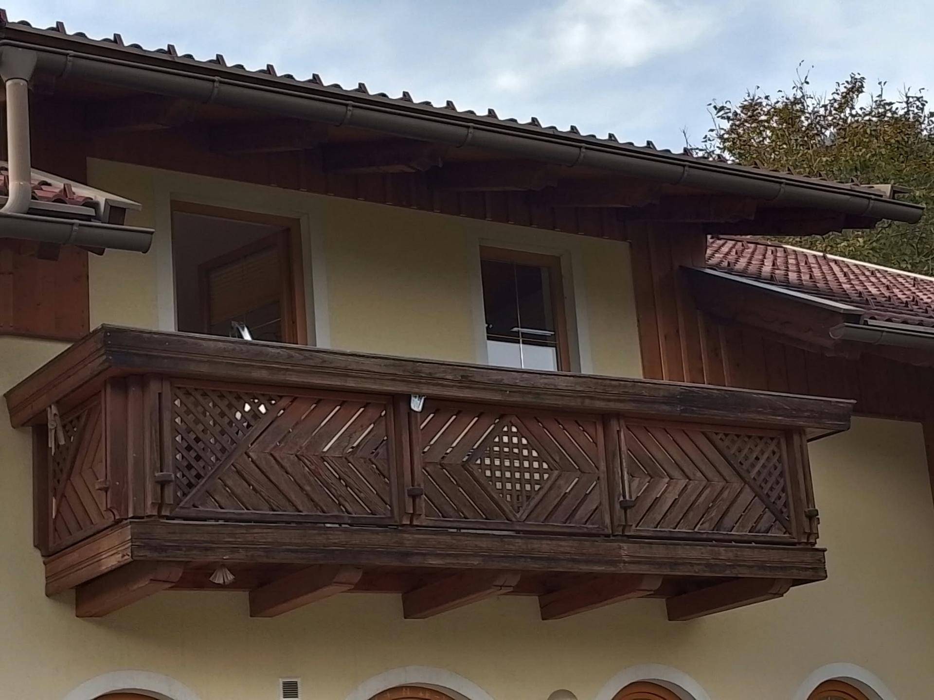 Traditioneller Holzbalkon an einer Fassade mit aufwendigen Schnitzereien und Ziegeln.