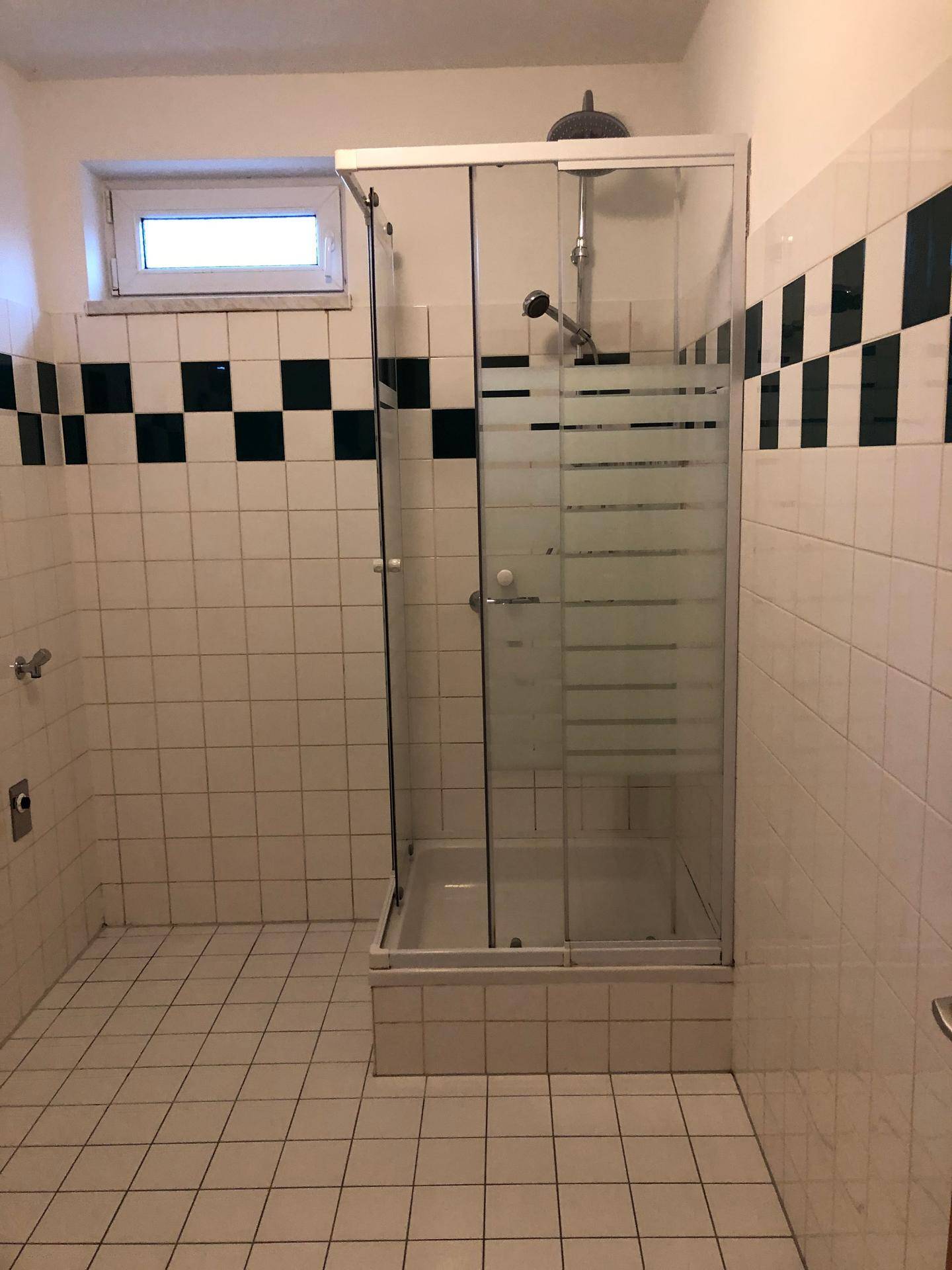 Badezimmer mit Duschkabine und charakteristischen weiß-grünen Fliesen, inklusive Fenster für Tageslicht.