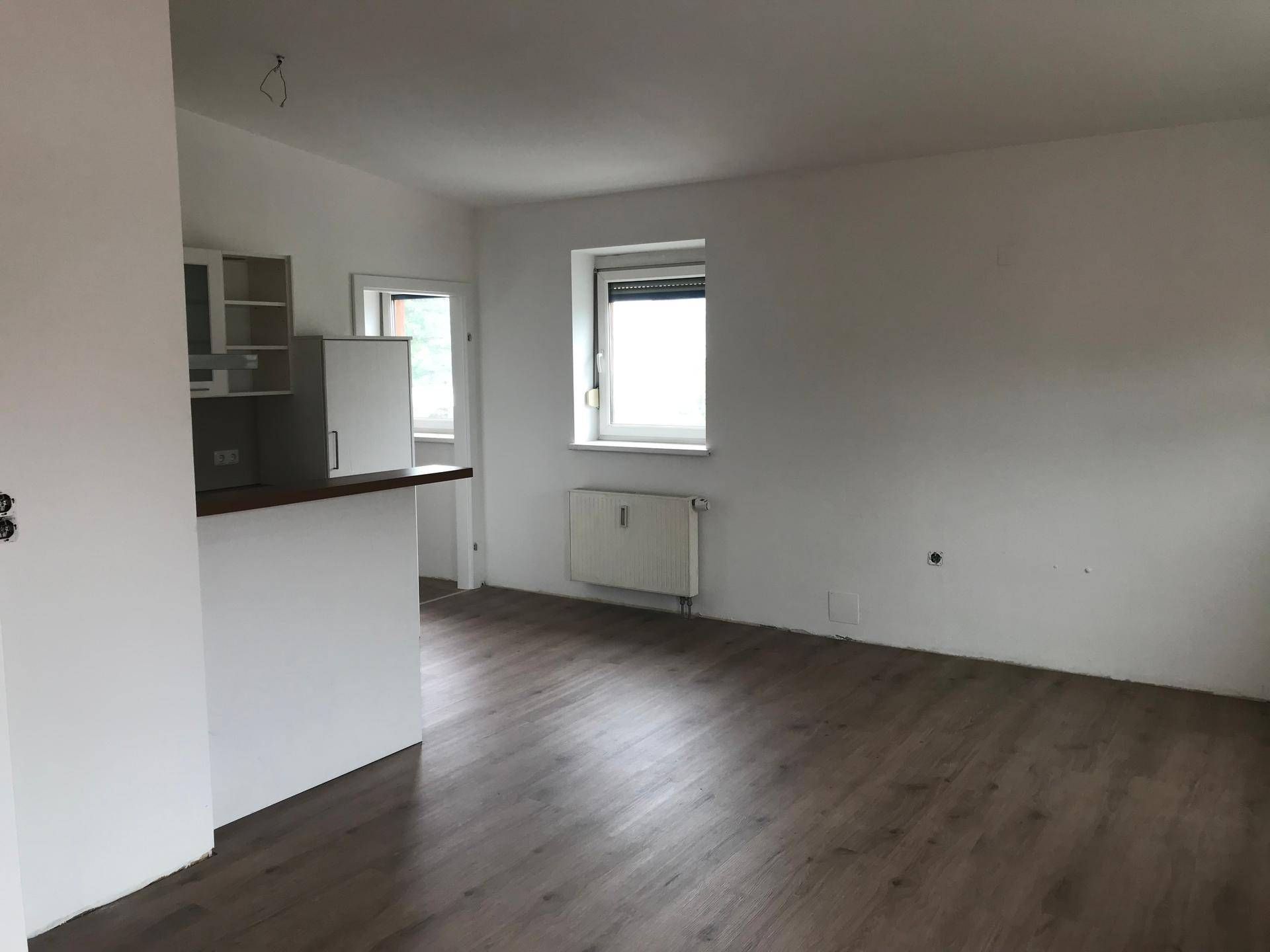 Heller, offener Wohnbereich mit integrierter Küchenzeile und Laminatboden, bereit zur individuellen Gestaltung.