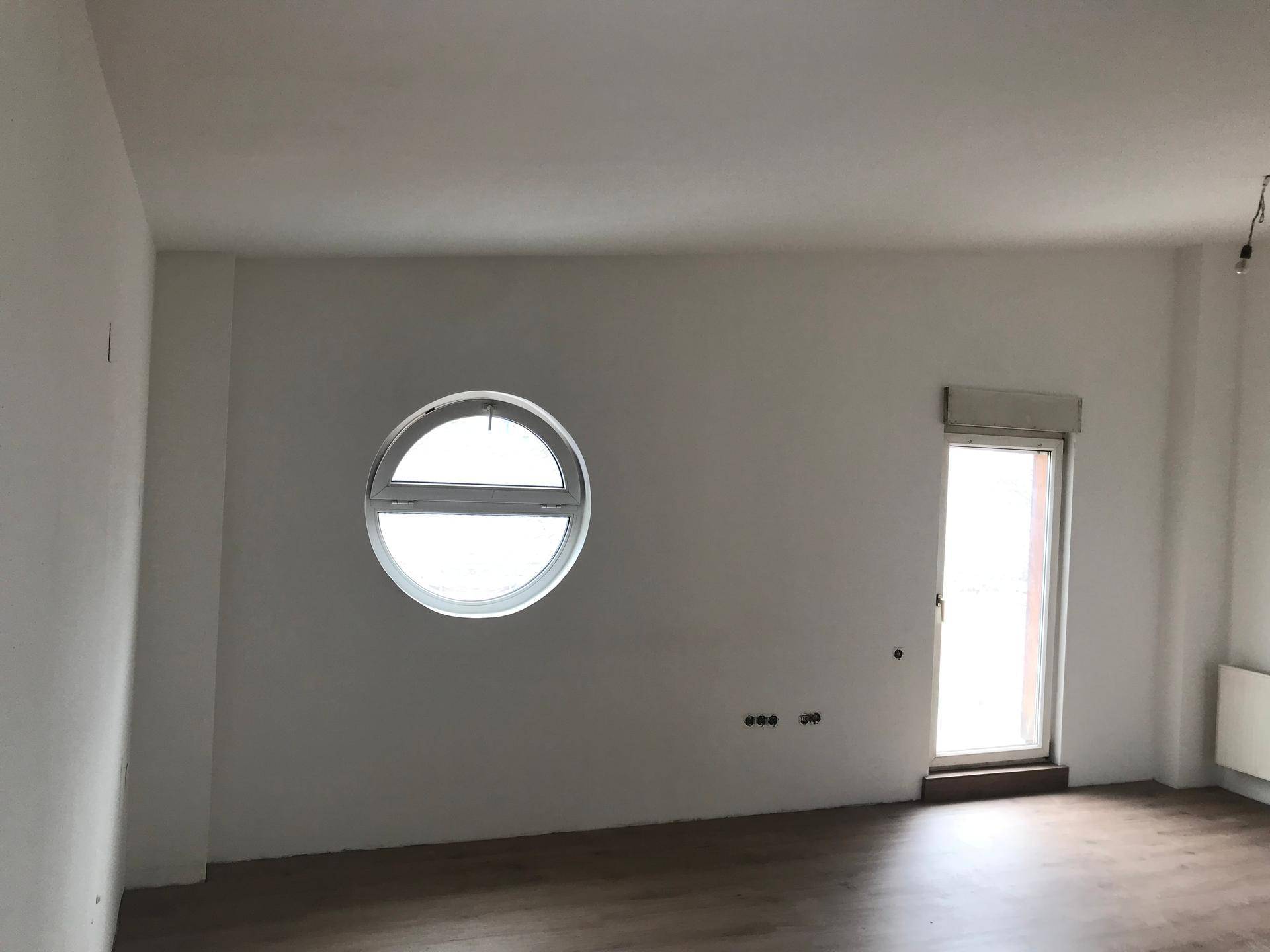 Leerer Raum mit einem markanten runden Fenster und Zugang zu einem Außenbereich, ausgestattet mit Laminatboden.