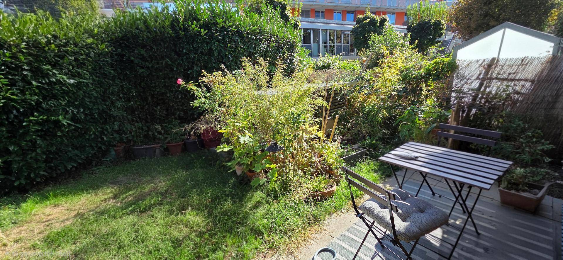 Grüner Gartenbereich mit Hecke, Rasenfläche und einer kleinen Sitzecke.